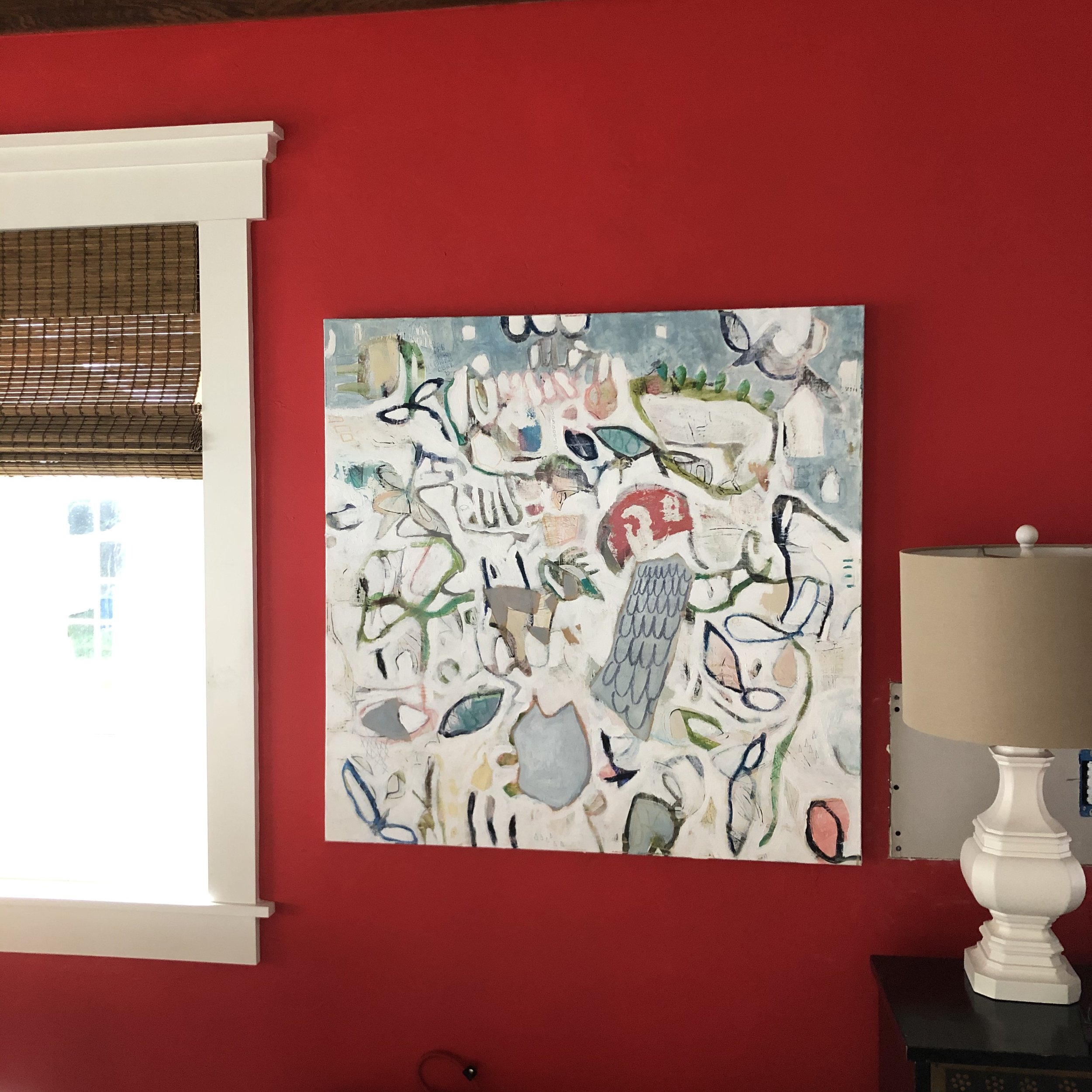 Colorful abstract painting with various shapes and lines on a white background displayed on a red wall.