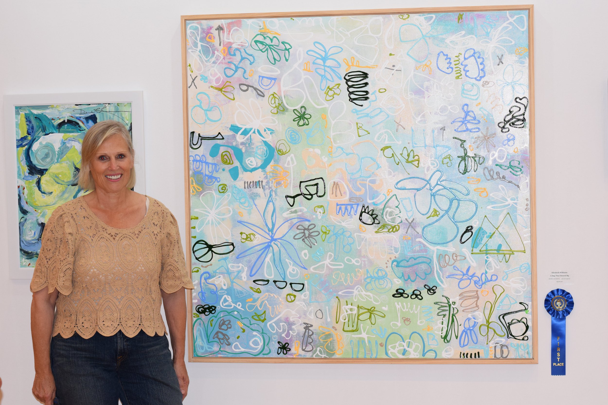 Elizabeth Williams standing beside Never Ending List, a large abstract mixed-media painting with layered colorful linework and pattern.