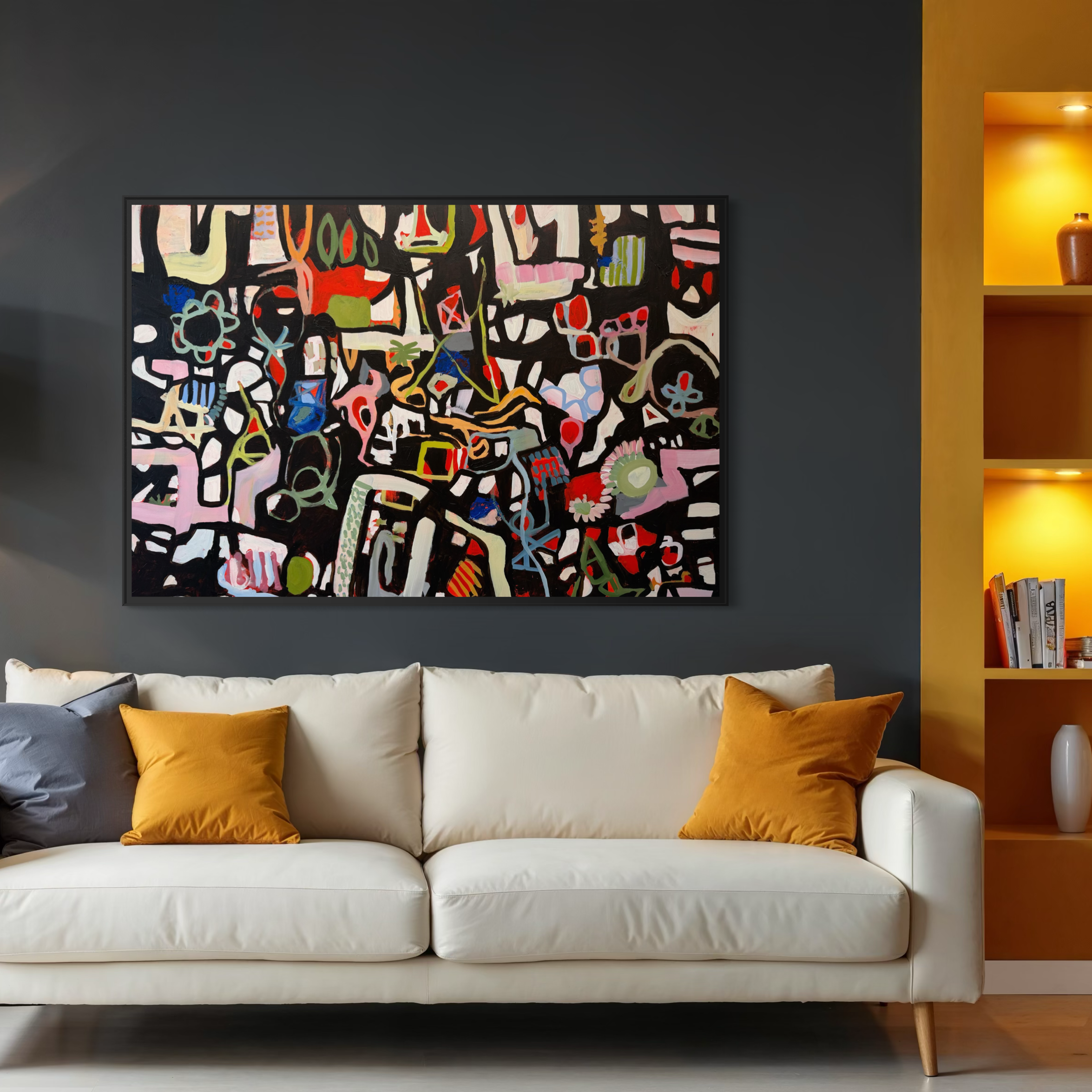 A white sofa with orange and dark gray pillows in front of a dark gray wall, with a colorful abstract art painting hung above it. To the right, a yellow wall with built-in shelves holding a pottery vase and books, illuminated by recessed lighting.