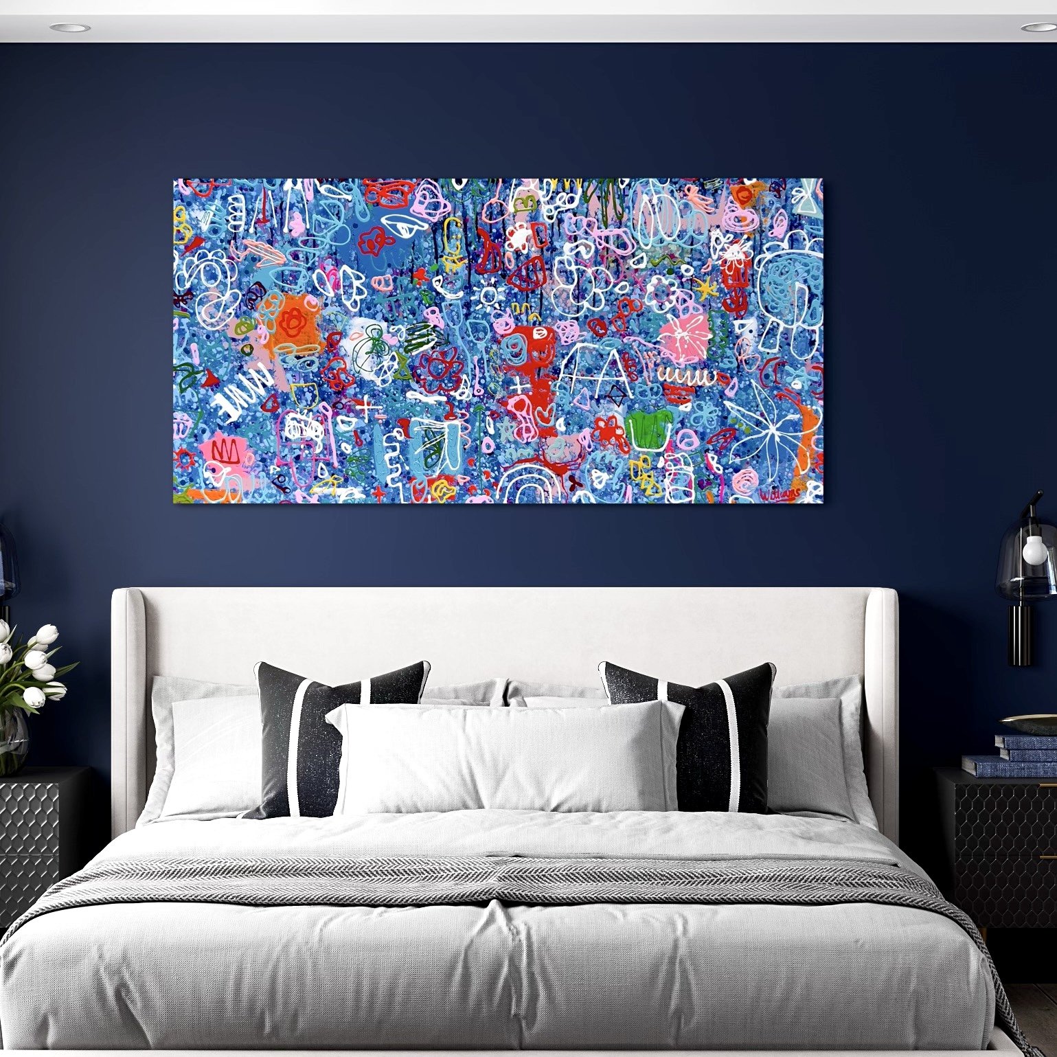 A colorful abstract painting with various doodles and symbols, hanging on a dark blue wall above a bed with white linens and black-and-white pillows.