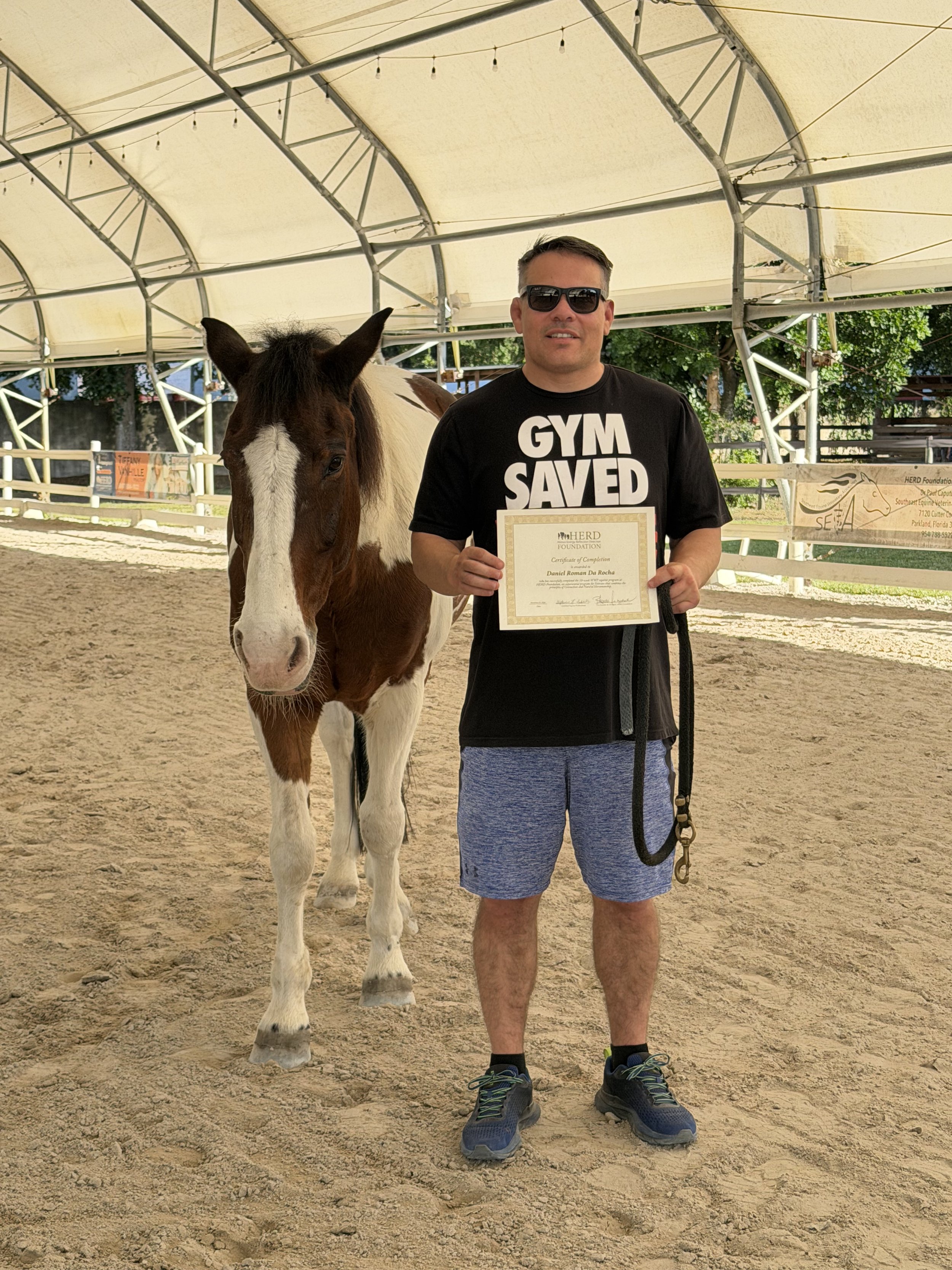 Man holding a certificate standing next to a horse in an indoor arena.