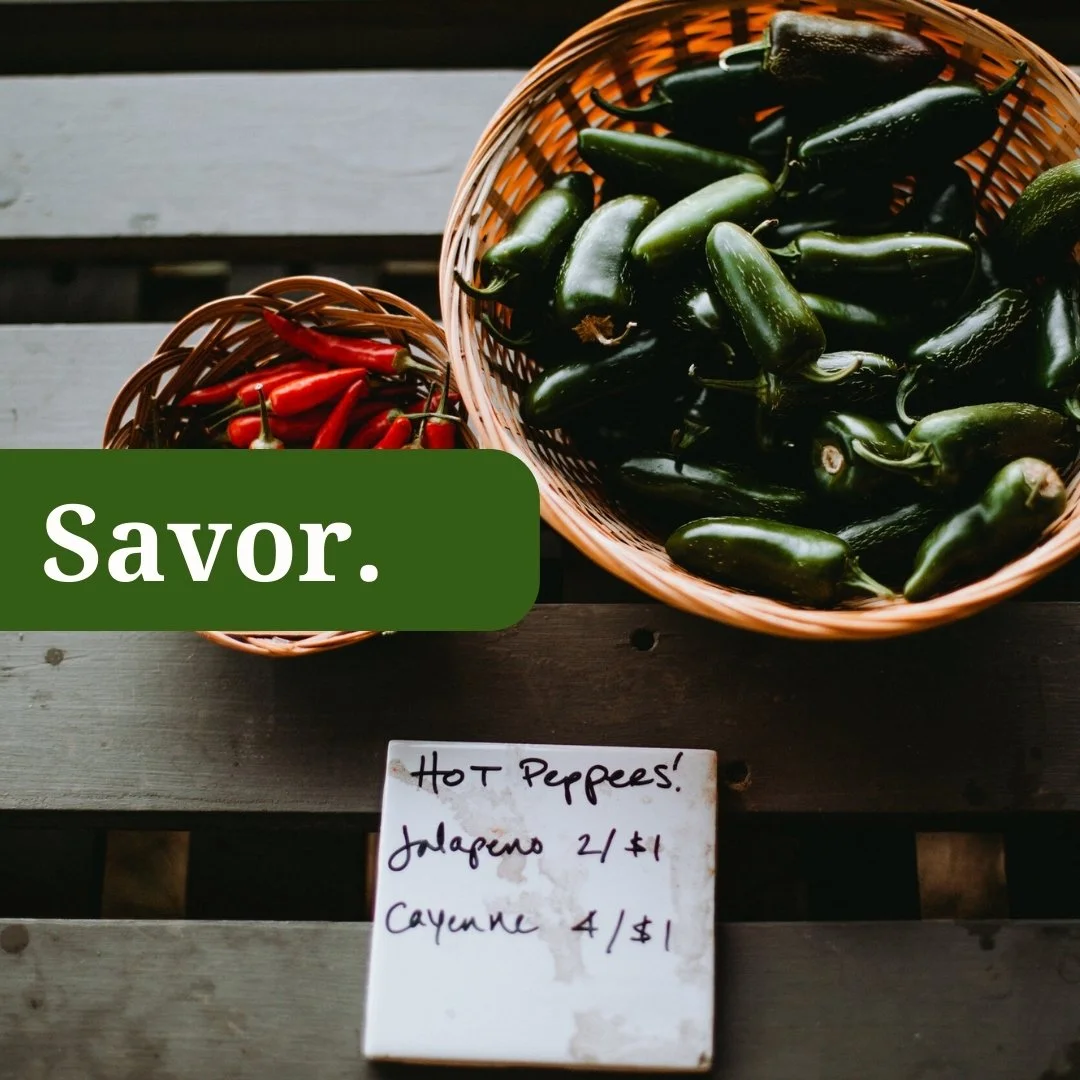Basket of fresh jalapeño peppers and a smaller basket of red chili peppers on a wooden surface. A handwritten sign with prices for hot peppers, jalapeños, and cayenne peppers is below the baskets. The word "Savor." is overlaid on the image in a green box.