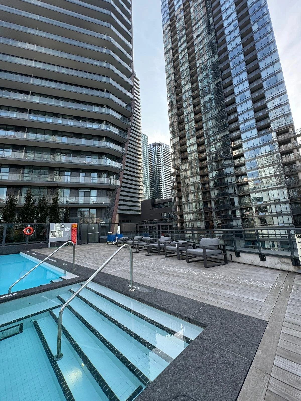 Urban rooftop pool area with pool, lounge chairs, and tall modern skyscrapers surrounding it.