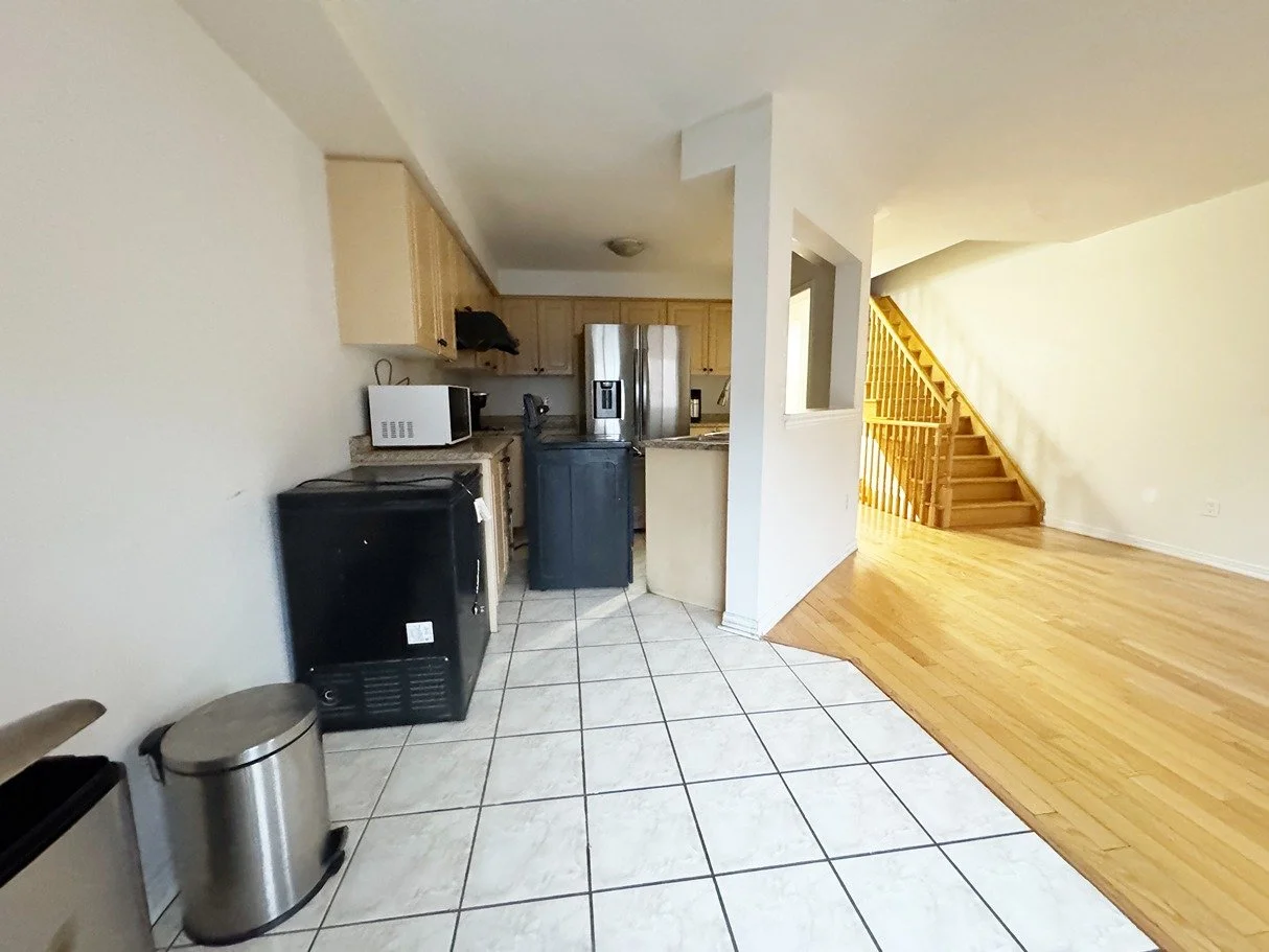Kitchen area with microwave, refrigerator, and small appliances, adjacent to a living room with hardwood flooring and a staircase.