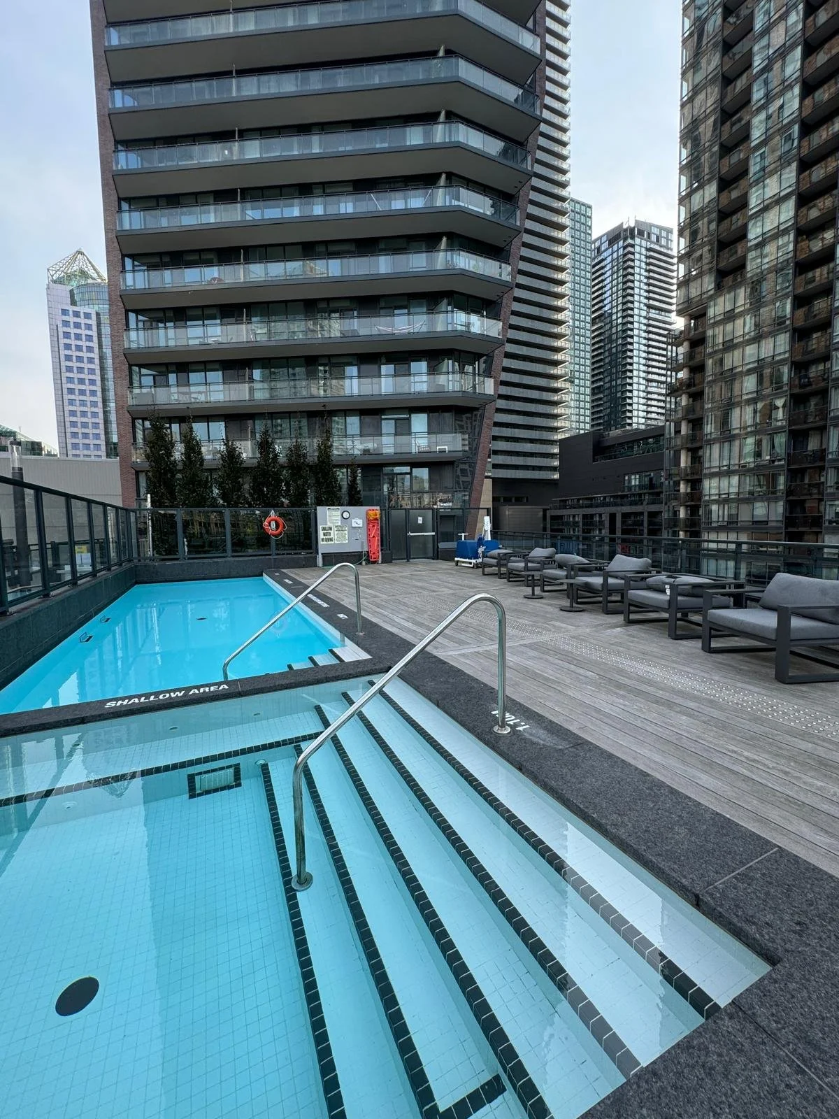 City rooftop pool area with blue pool, lounge chairs, and modern high-rise buildings in the background.