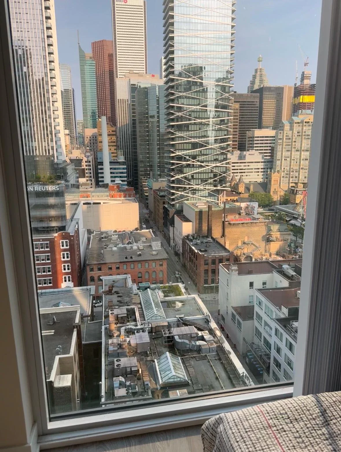 View of downtown skyscrapers through a large window, including the BMO building, various modern glass and brick buildings, and rooftop HVAC units in the foreground.