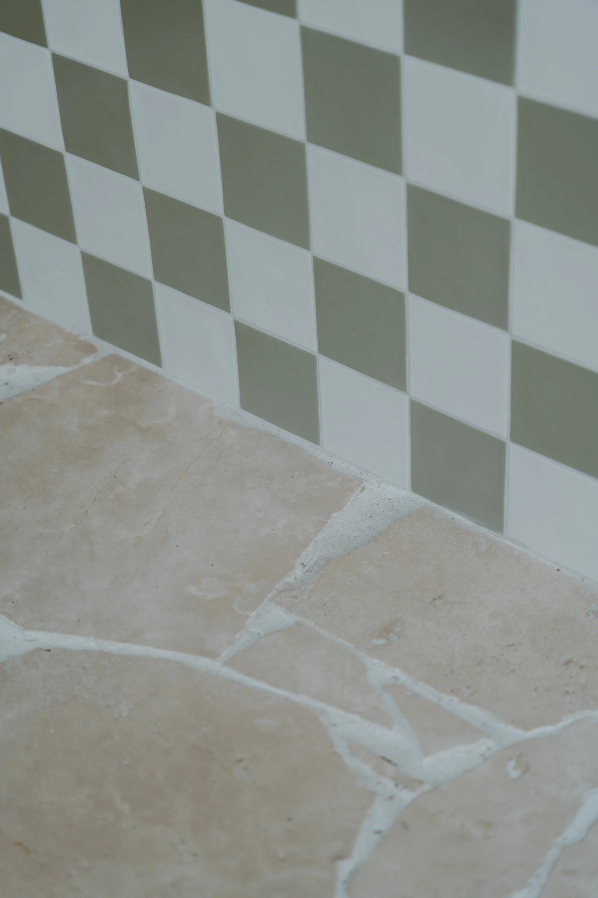 Close-up of a tiled wall with a checkered pattern of white and gray tiles above beige stone flooring.