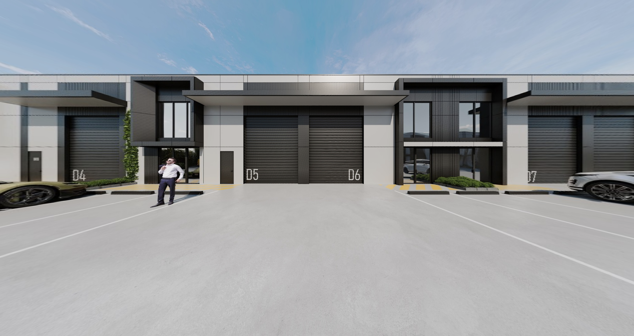 View of a modern commercial building with black metal roll-up doors, large glass windows, and a parking lot in front with several parked cars, blue sky, and a man standing near a car talking on the phone.