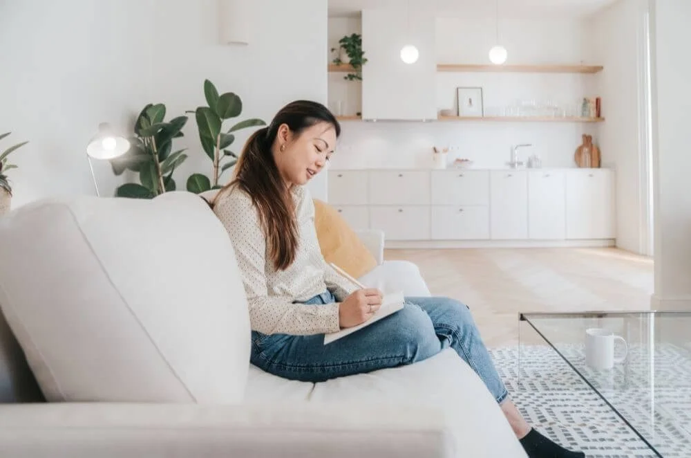 Woman journaling on a couch, reflecting and reconnecting with emotions after childhood emotional neglect