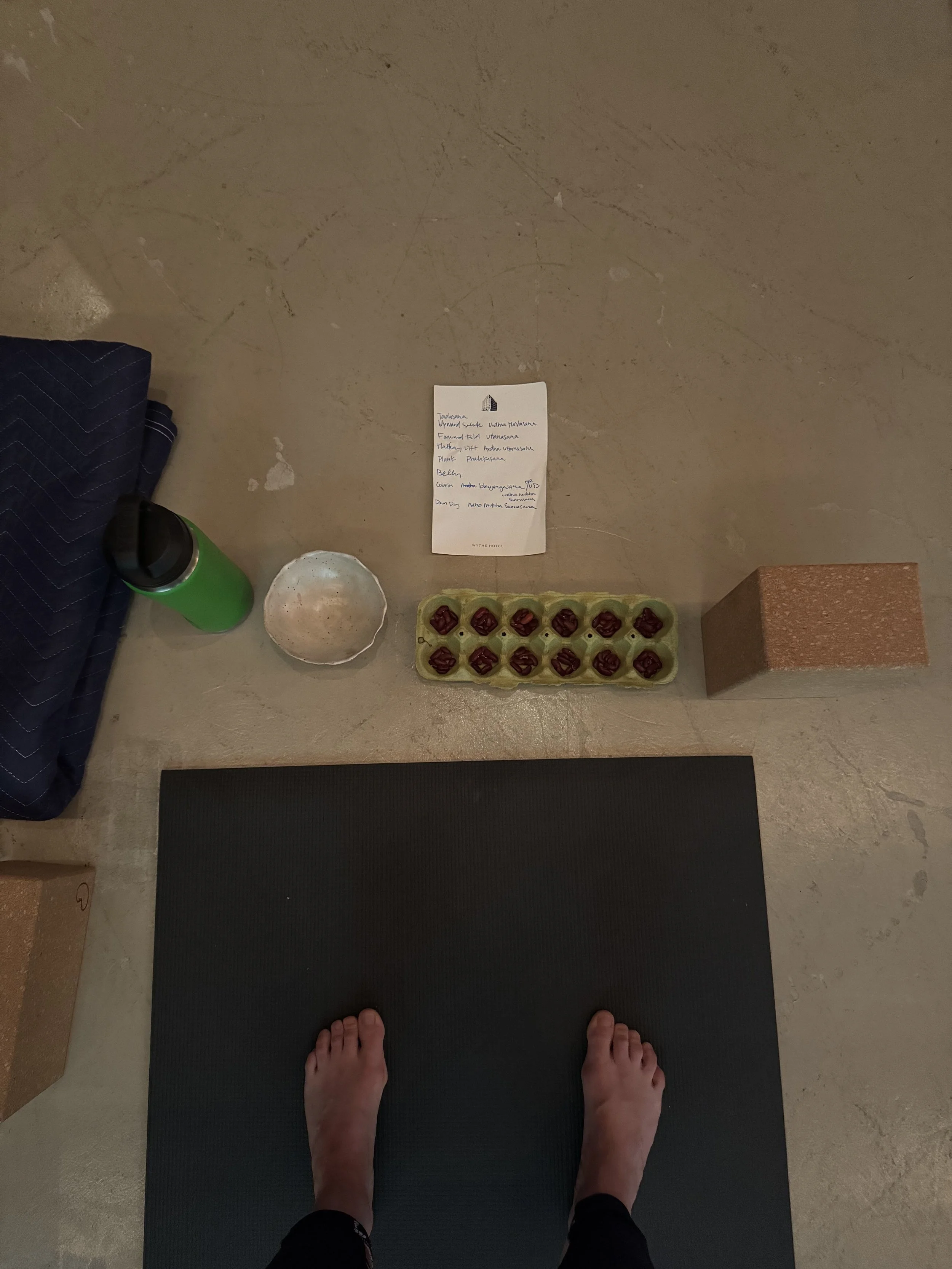 clare standing at top of mat with blocks, water bottle, script and beans for counting out 108 sun salutations