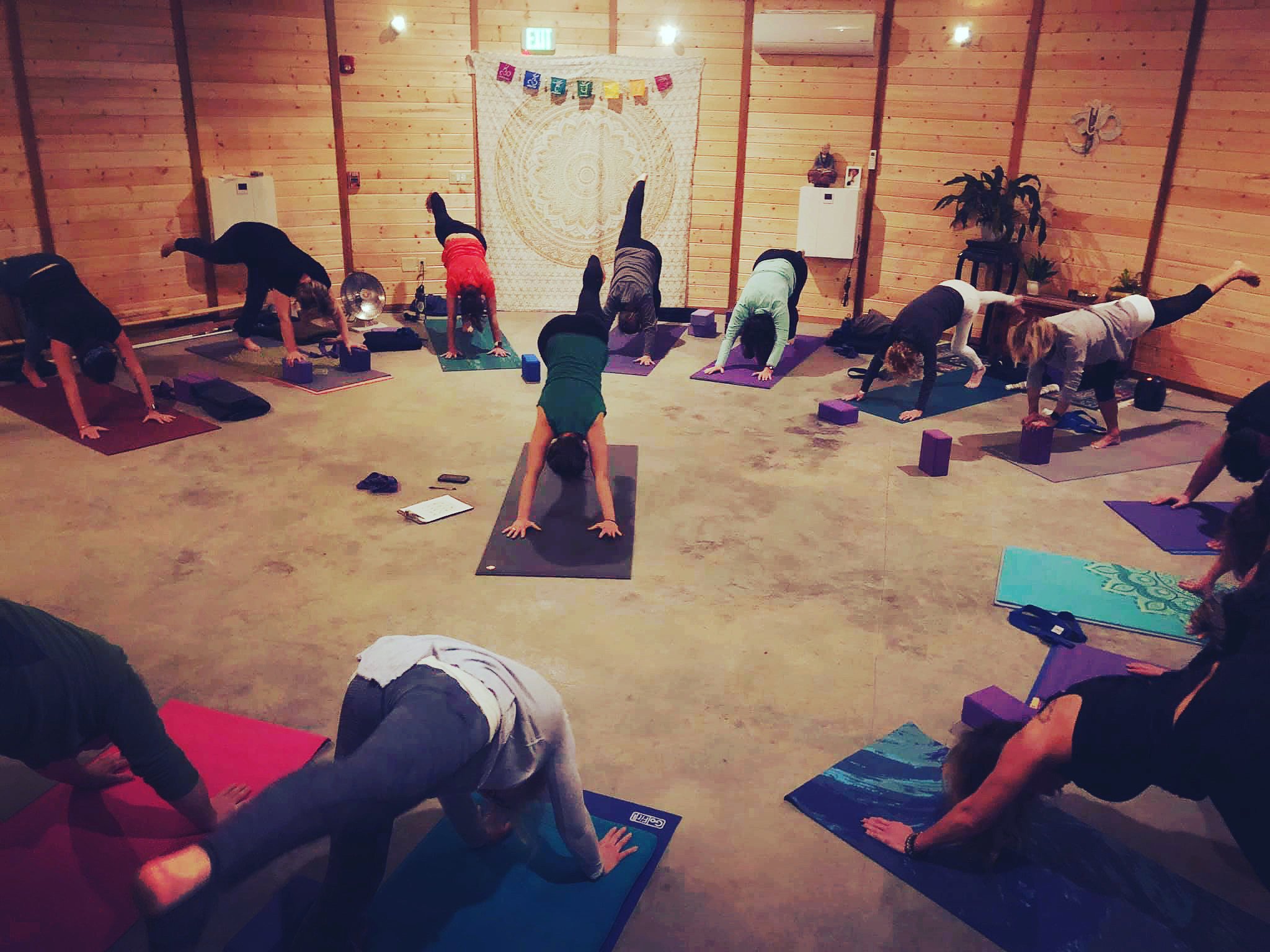 yoga class in the round with clare teaching in the center. everyone is in 3 legged dog pose