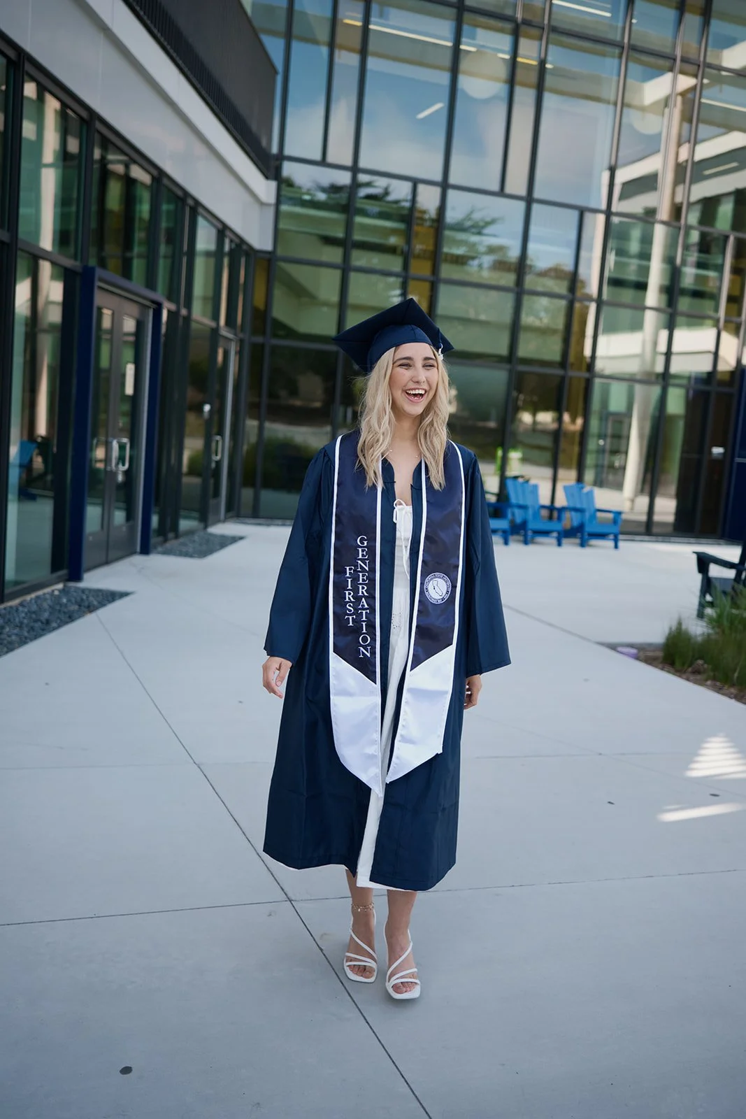 a young female wearing her cap and gown at CSU Monterey Bay in front of the student union building