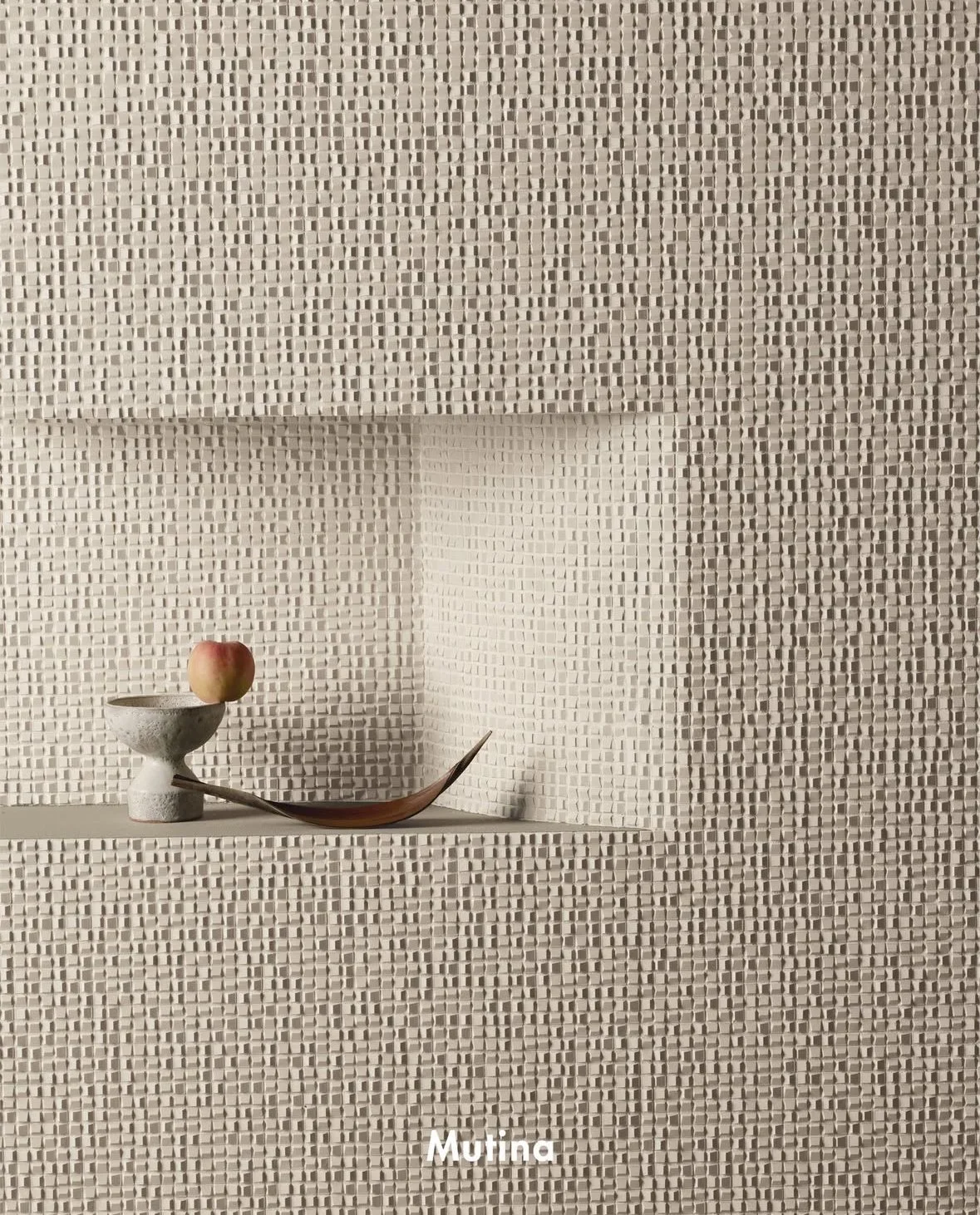 Minimalist display with a textured beige wall, a small white ceramic bowl, an apple, and a curved wooden object.