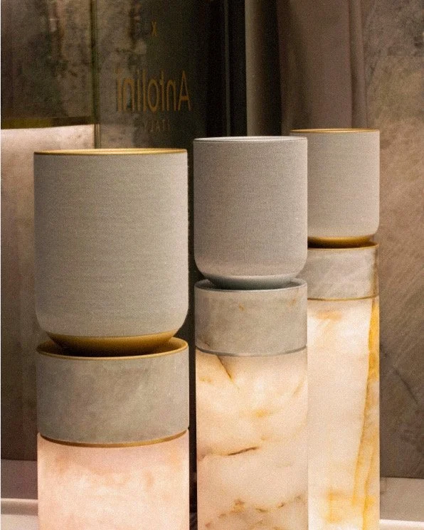 A collection of six modern planters arranged on top of marble pedestals inside a store or gallery, with a reflective glass window in the background.