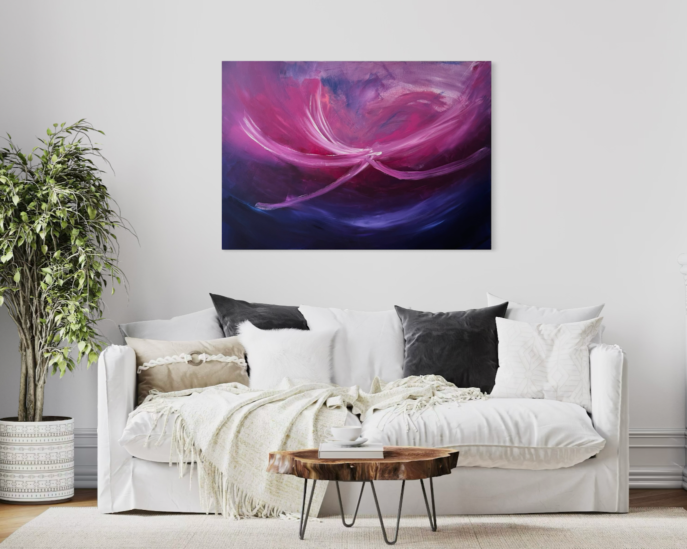 Ein modernes Wohnzimmer mit einem weißen Sofa, dunklen und hellen Kissen, einer Decke, einem kleinen runden Holztablett, einer weißen Wand mit einem großen abstrakten Kunstwerk in Pink, Lila und Blau, und einer topfpflanze auf der linken Seite.