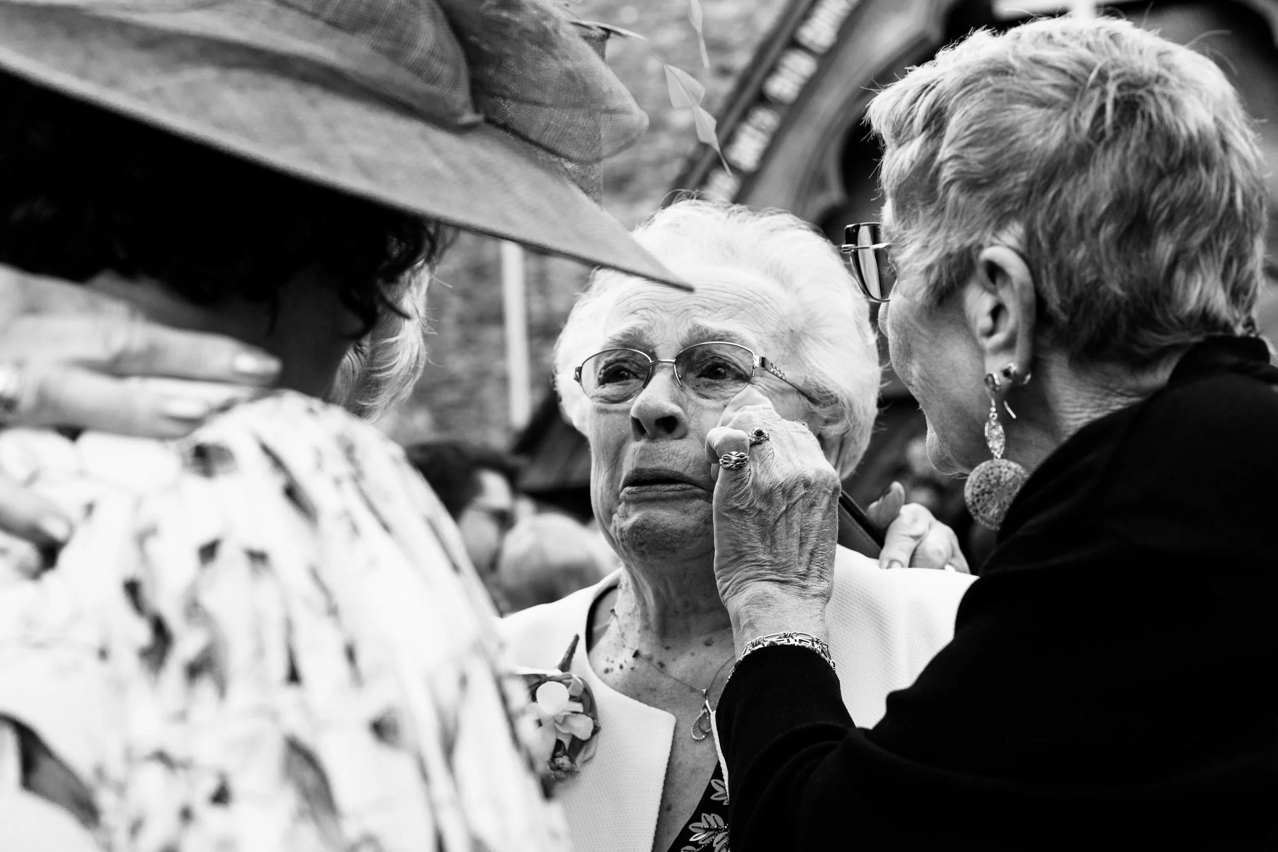 Black and white documentary-style wedding photo of a grandmother crying with emotion after the ceremony, capturing a powerful and intimate family moment. 