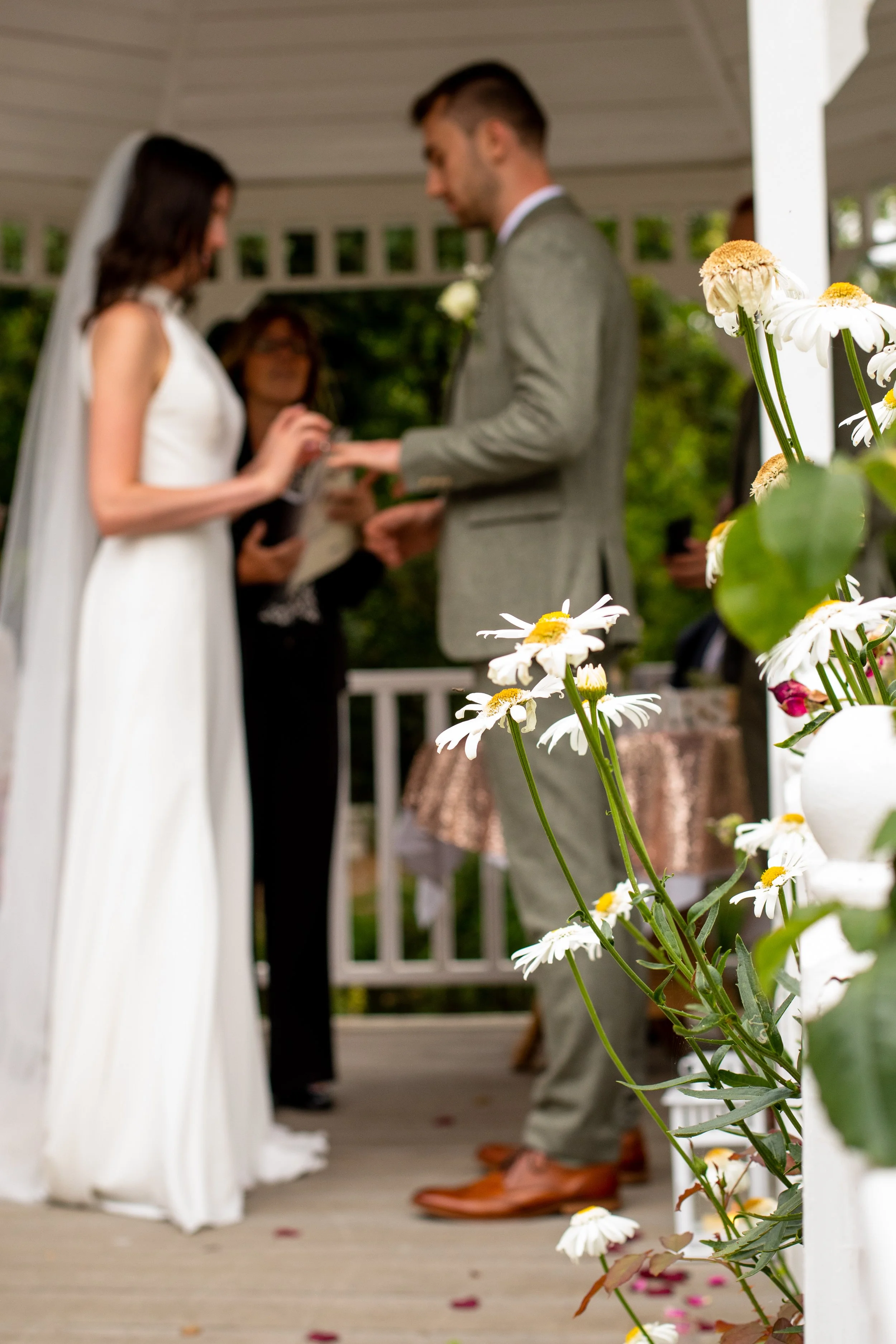 Bride and groom exchanging vows during an outdoor wedding ceremony, with floral decorations in the foreground.