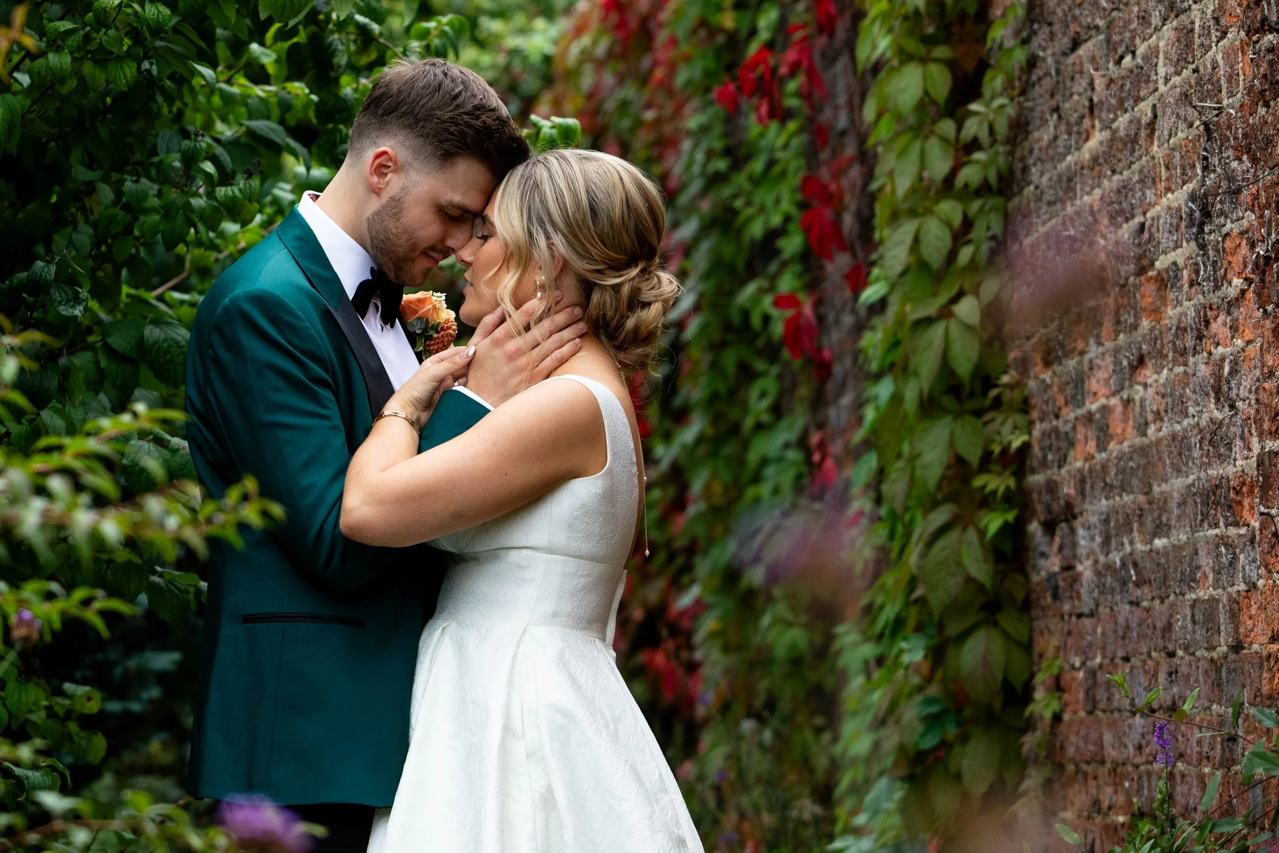 Couple embracing at Gaynes Park wedding venue in Essex, surrounded by beautiful ivy-covered walls in a romantic countryside setting. 
