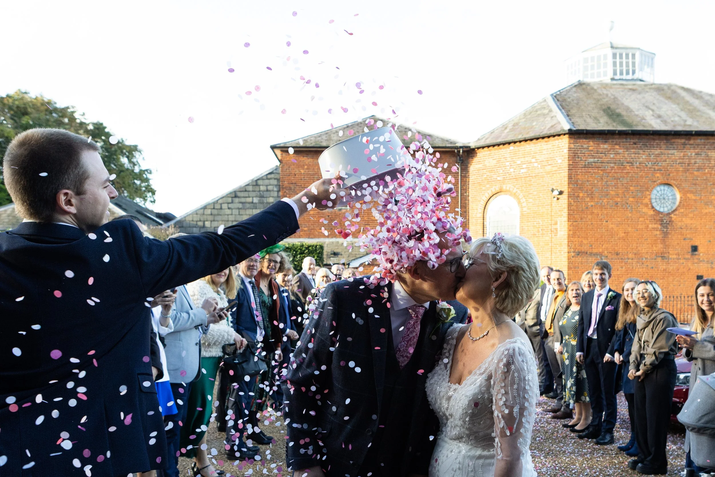 Guest pouring a bucket of confetti over the couple at Kings Chapel in Amersham. 