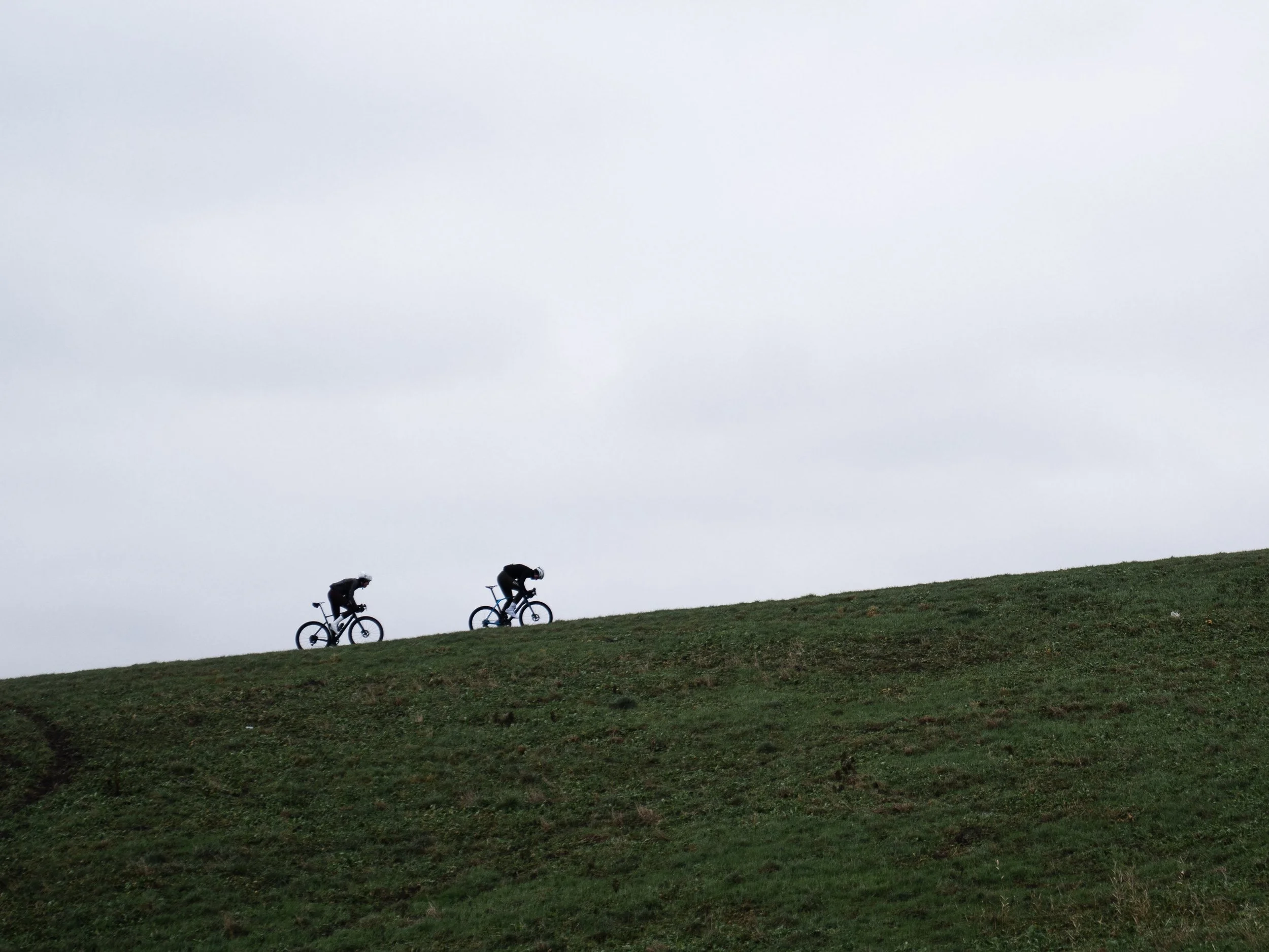 Two road cyclists sprinting up the Maeslantkering storm surge barrier hill near Maassluis, one of the largest moving structures in the world.