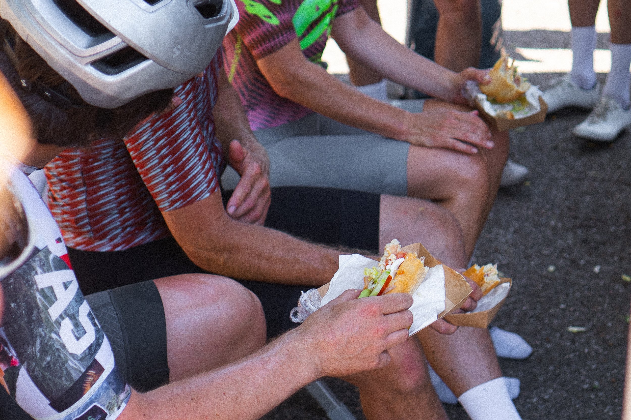 Cyclists ating heavy sandwhiches during a mid-ride stop, the kind that slows you down for the next hour.
