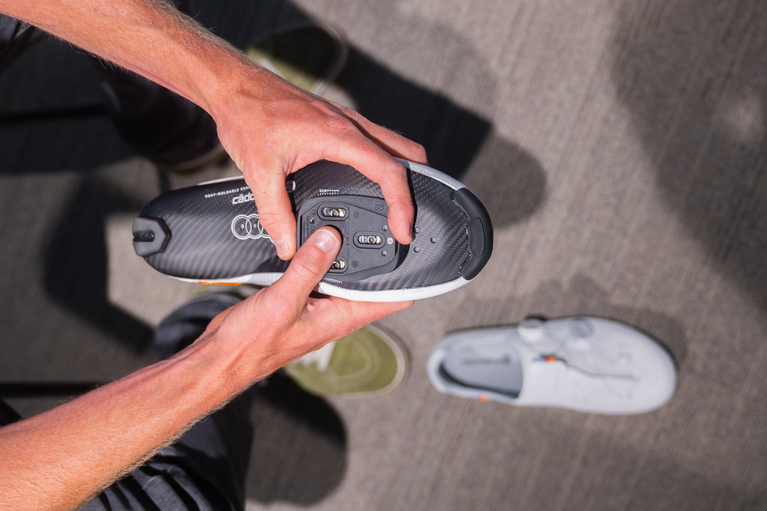 Bike fitter Peter Kraaijvanger holding a Cadomotus carbon shoe sole up, showing the Wahoo Speedplay base plate with its adjustment slots and position markings before the cleat is fitted.