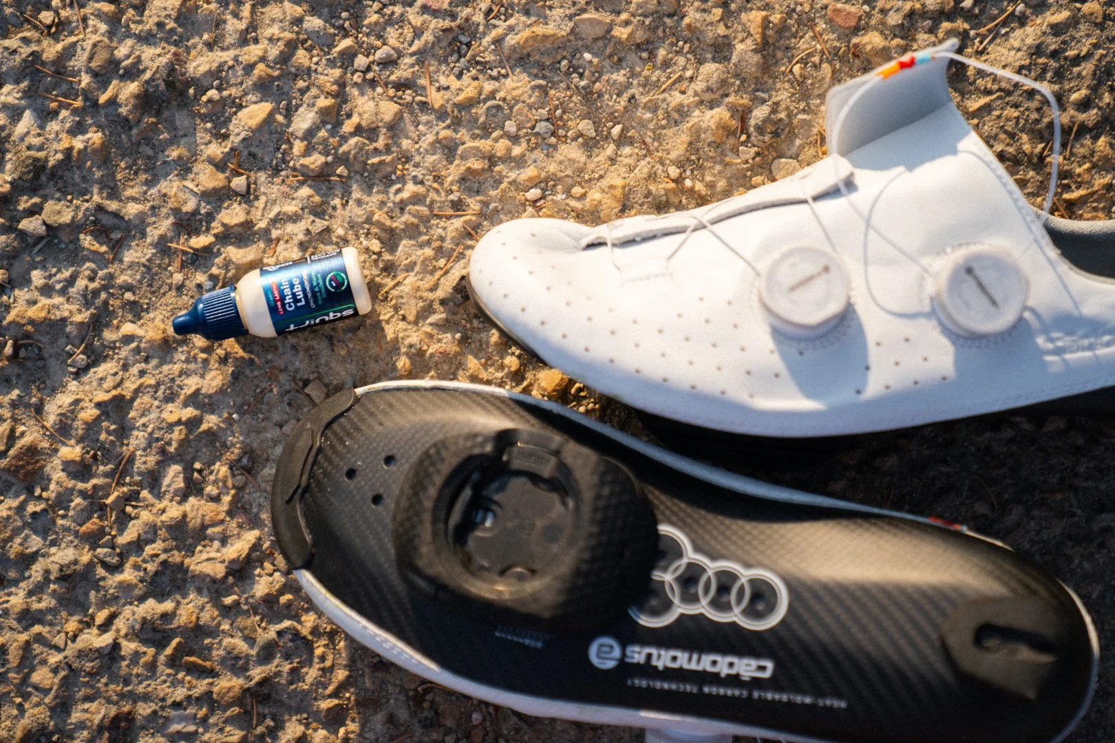 A pair of Cadomotus road shoes next to a bottle of Squirt chain lube, with the Wahoo Speedplay cleat visible on the upturned sole.