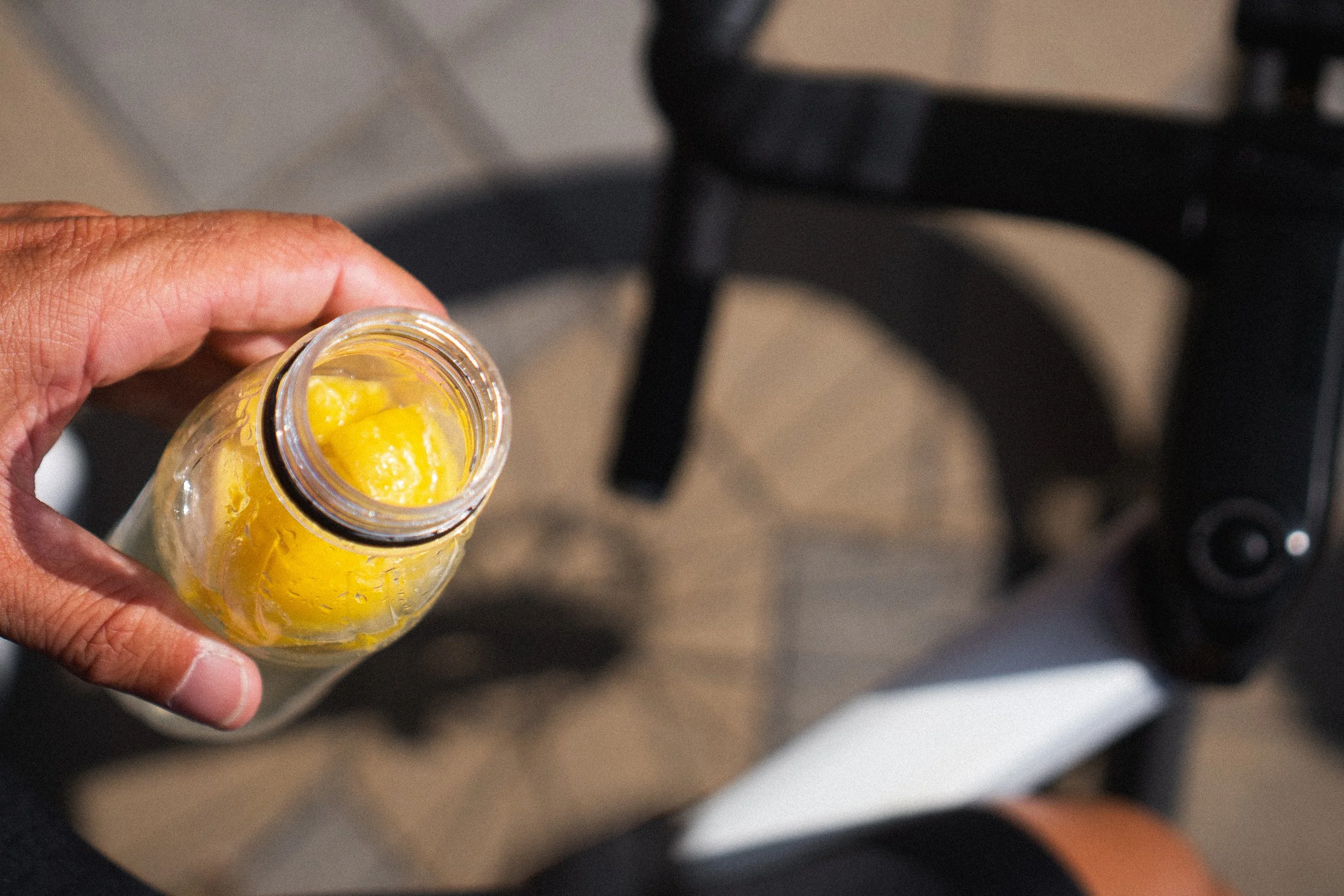Cyclist holding a small bottle of fresh orange juice at a mid-ride stop with a road bike in the background.