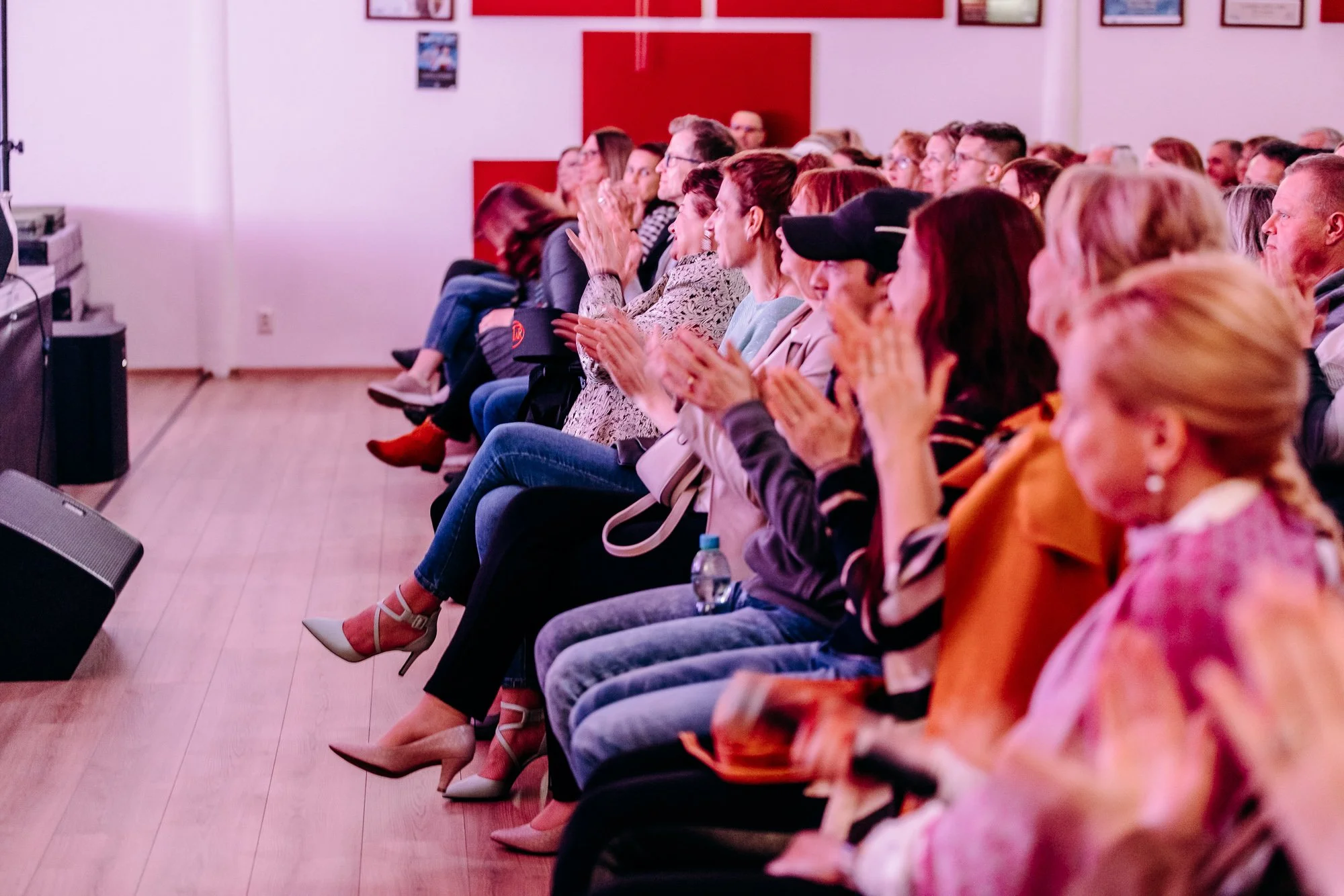 Audience members seated in a theater, clapping and watching a performance or presentation on stage.