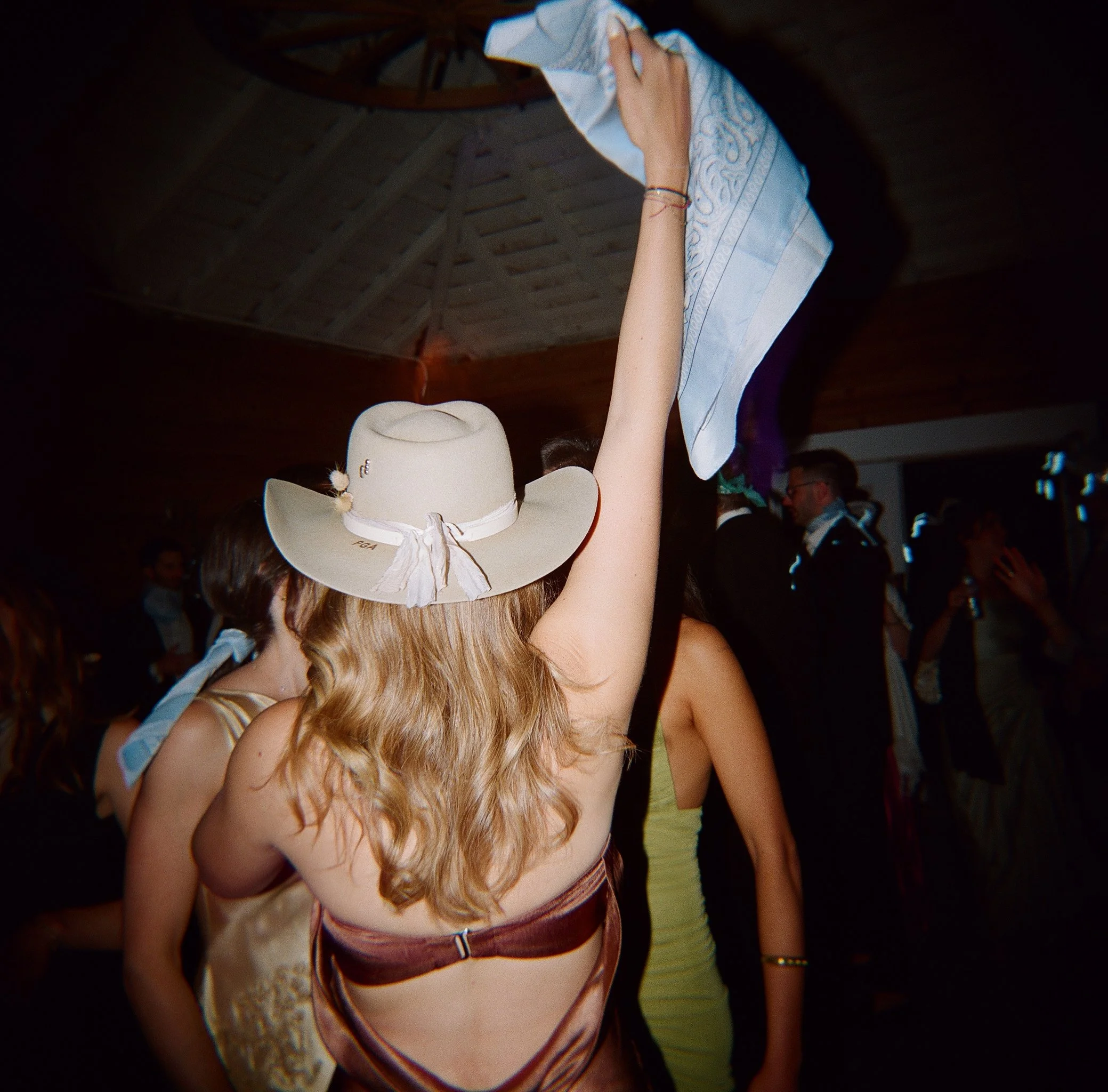 Wedding reception dancing inside Stonepine Estate, guest in cowboy hat raising a bandana on the dance floor, film wedding photography by Radostina Boseva Carmel Valley