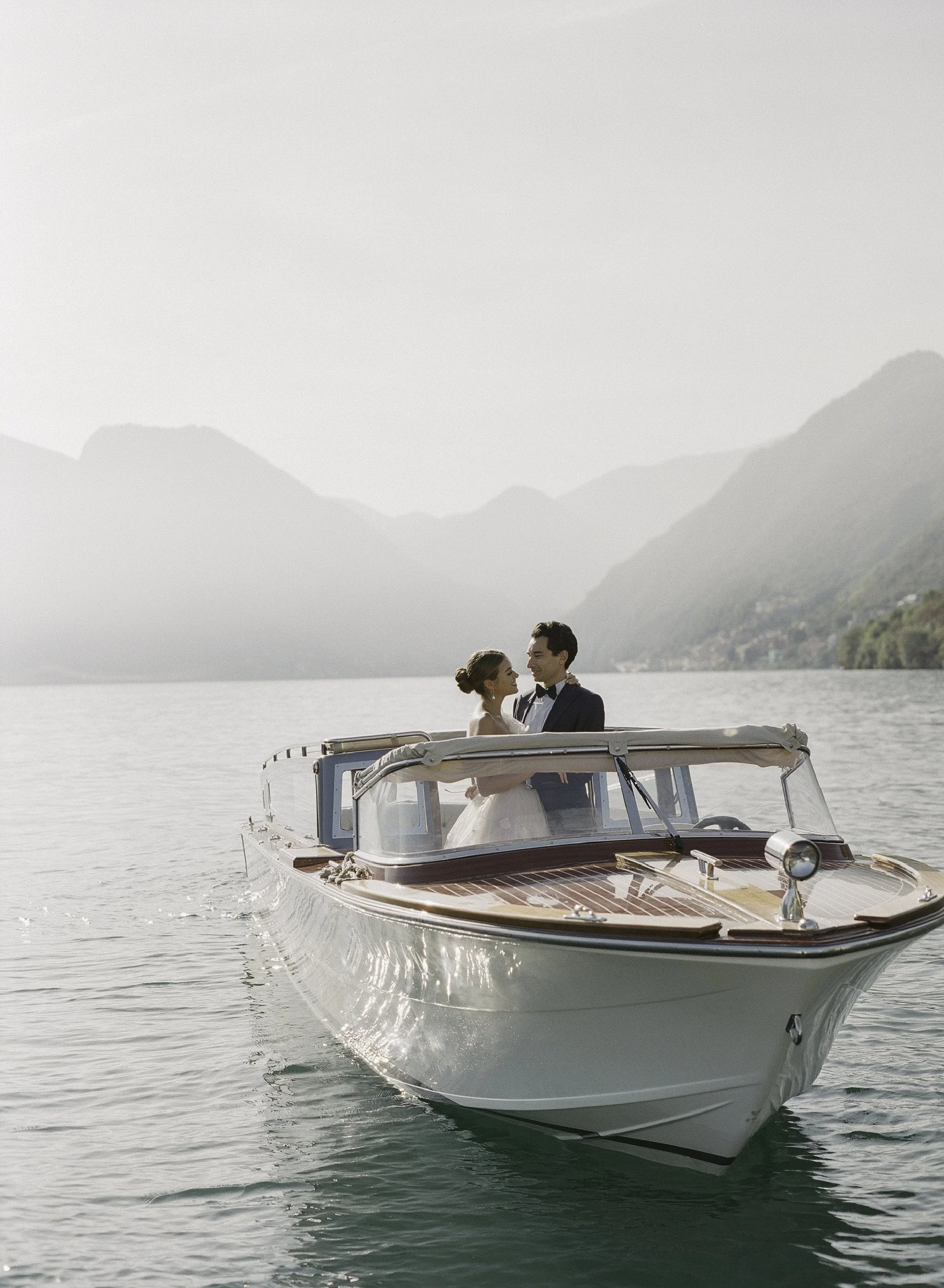 couple embracing aboard a vintage riva boat on lake como, misty mountains behind · italy elopement · documentary film photography by radostina boseva