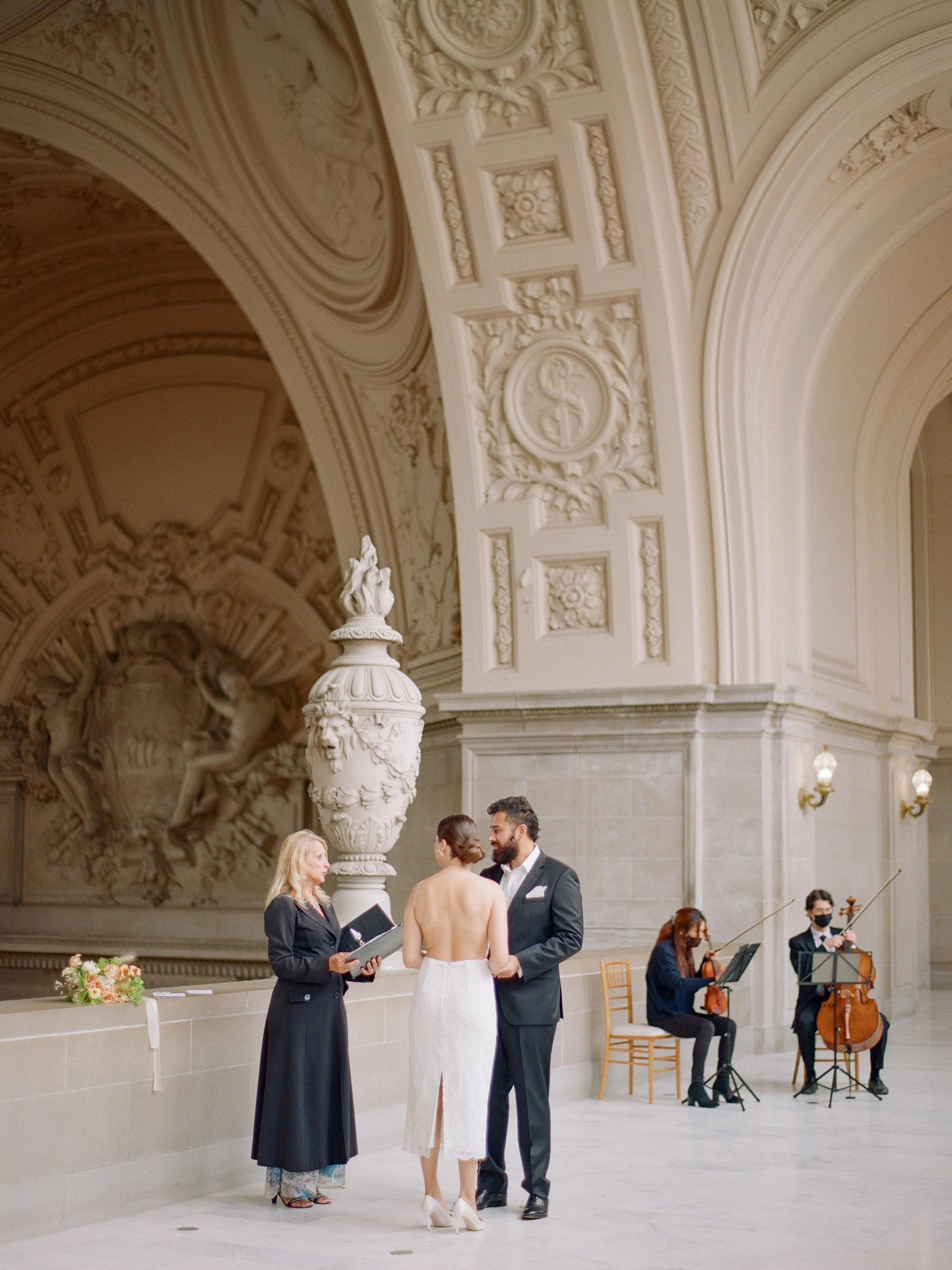 Couple exchanging vows at San Francisco City Hall with a string quartet playing behind them, film wedding photography by Radostina Boseva