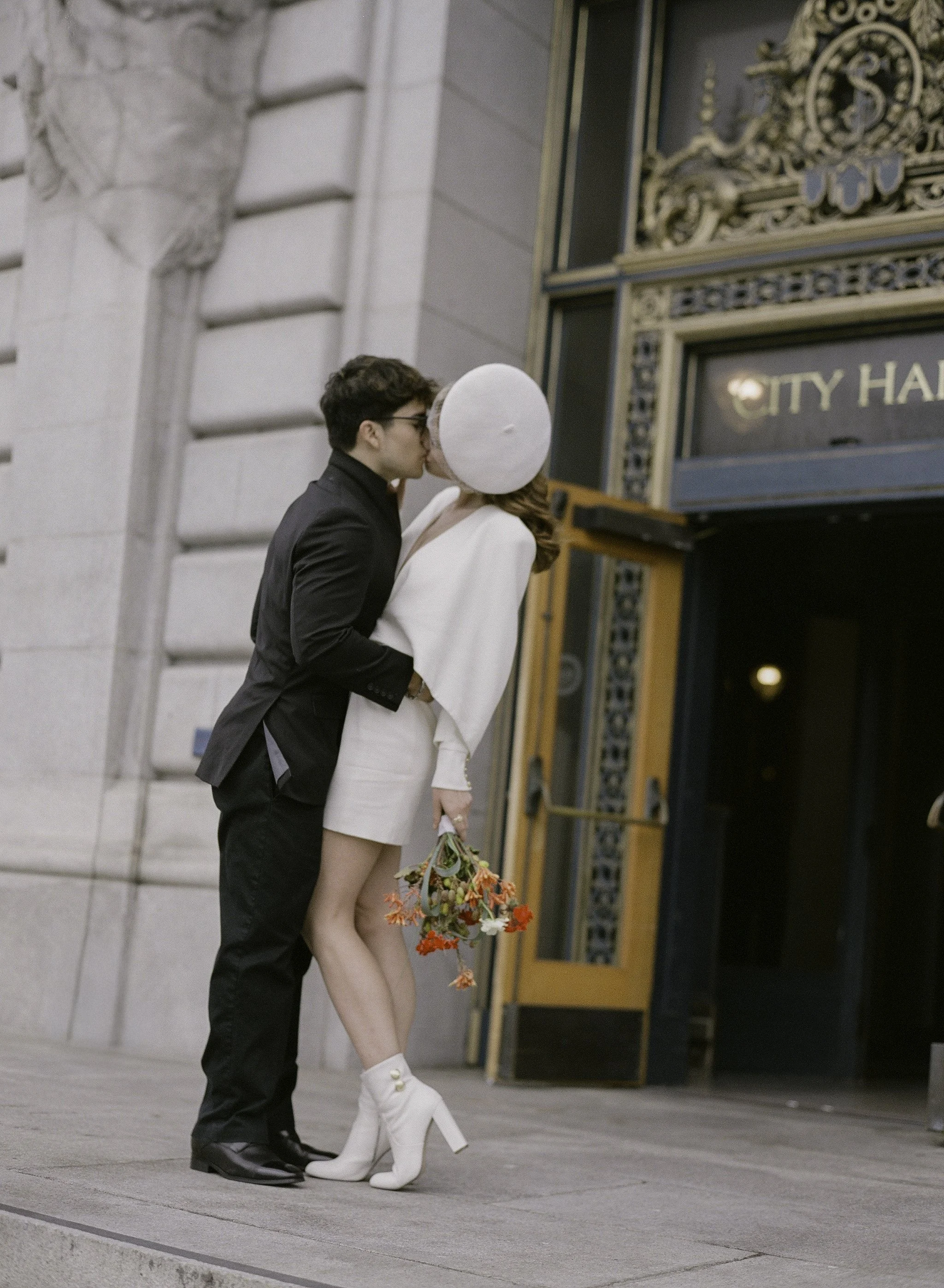 bride and groom kissing behind a white balloon at the san francisco city hall entrance, orange bouquet in hand · editorial film photography by radostina boseva