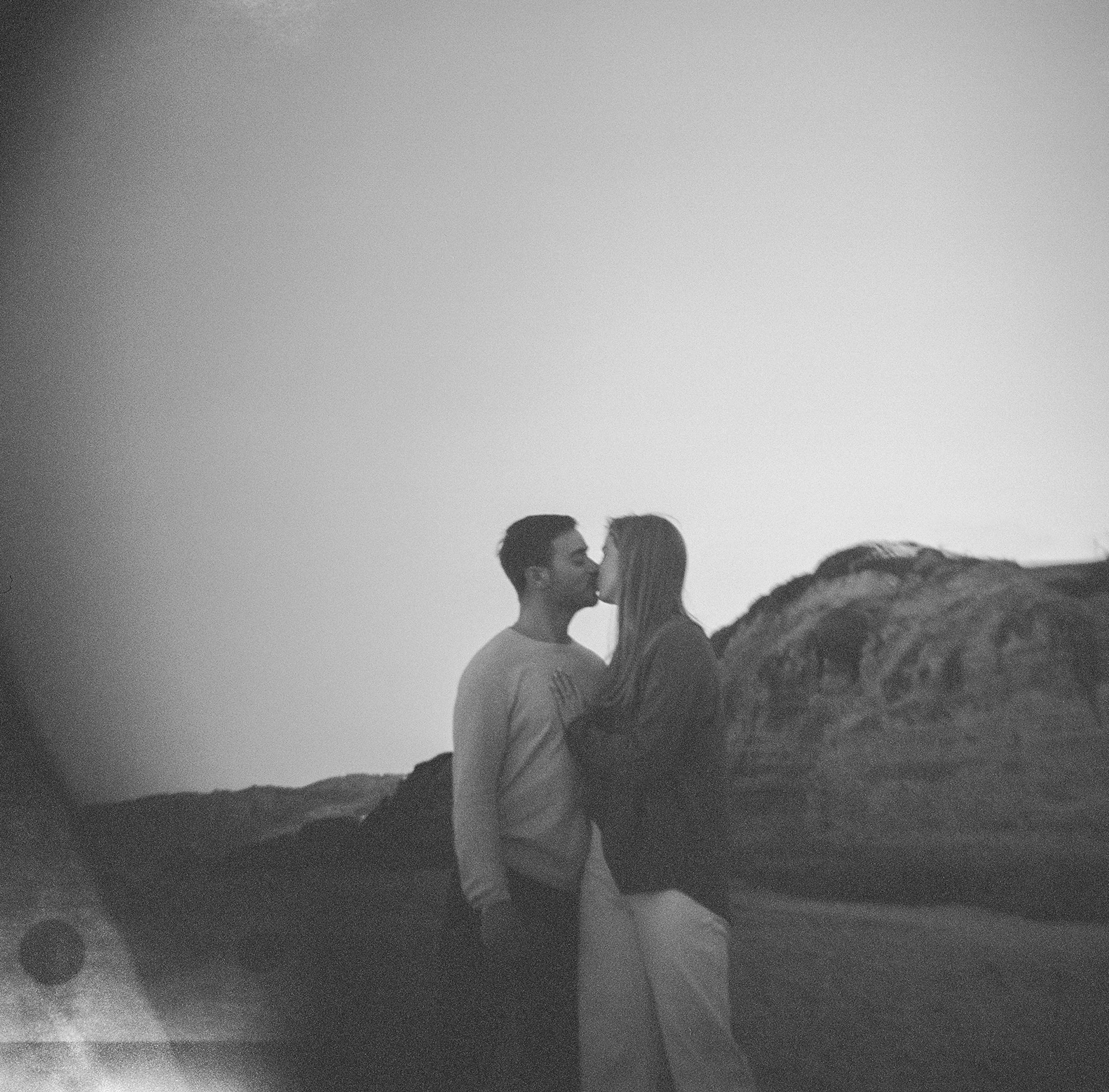 Black and white film portrait of couple almost kissing against coastal cliffs in Mendocino