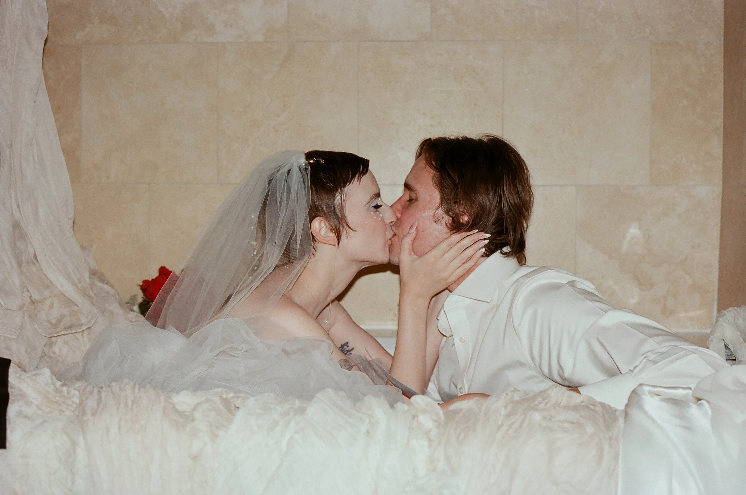 Bride and groom sitting in a tub with a sea of gauze and gown, kissing.