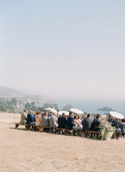 Outdoor wedding ceremony on coastal bluff overlooking the Pacific, guests seated on wooden benches, photographed on film in Mendocino