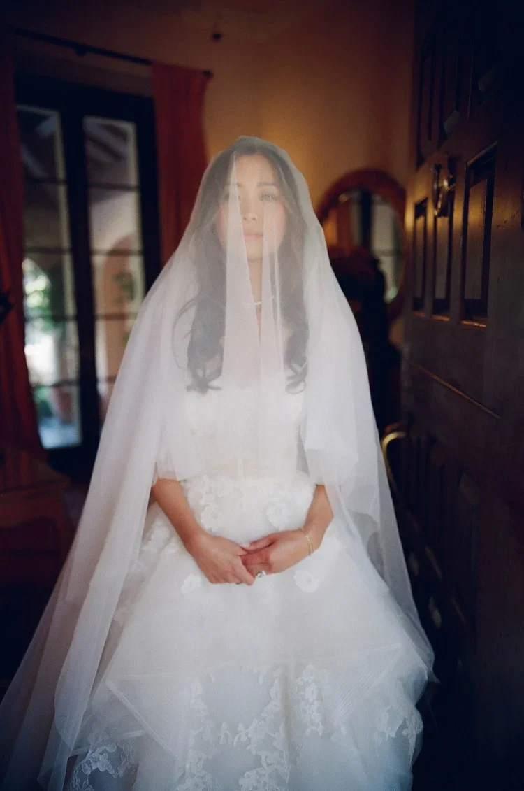 Bride standing in warm interior light with full veil covering her face, film portrait, destination wedding photographer Mediterranean