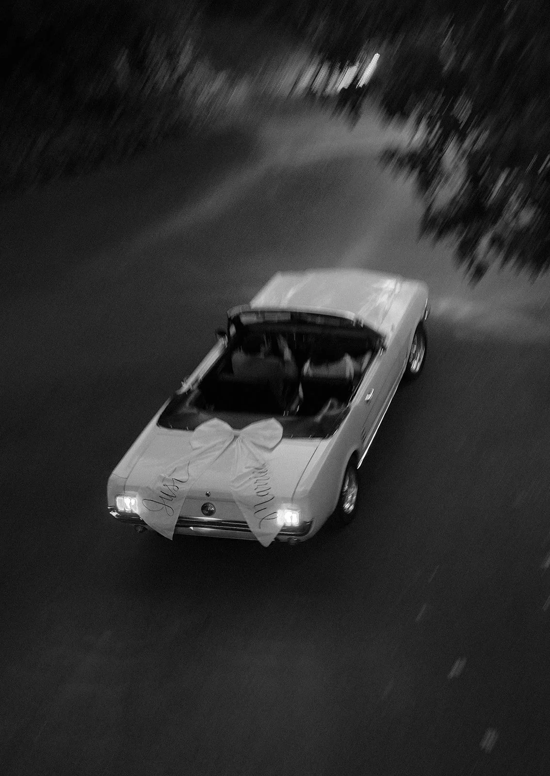 overhead view of a just married vintage mustang convertible with a white bow, driving into the dark, motion blur on film