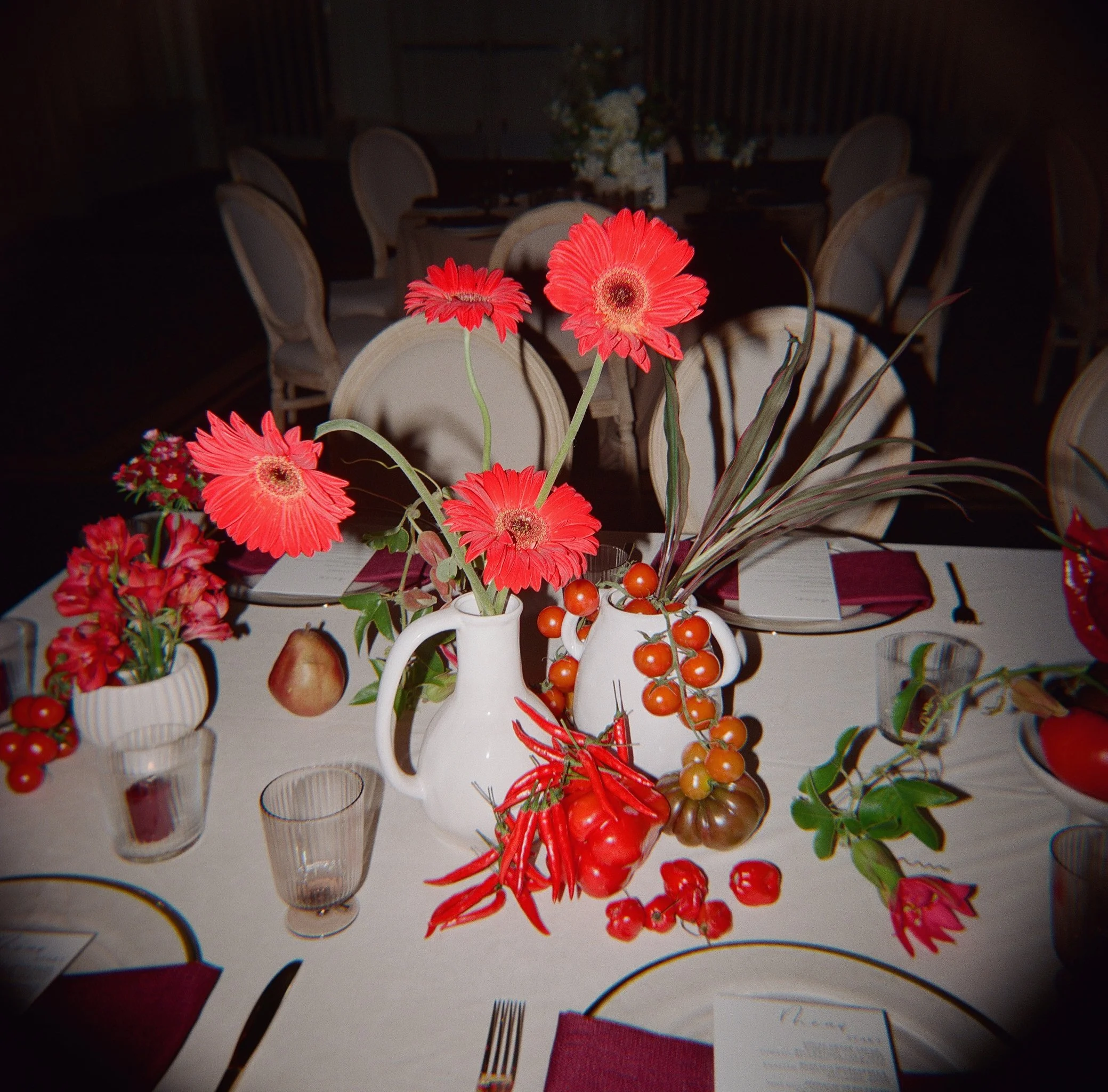 Wedding reception table detail with red florals and seasonal produce — film wedding photography, Los Angeles