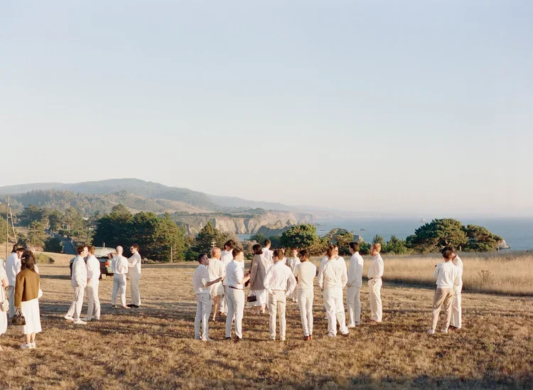 Wedding guests in white gathering in golden field overlooking the coast at Cuffey's Cove, photographed on film in Mendocino
