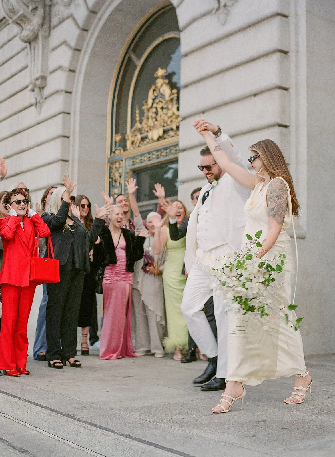Bride and groom exiting San Francisco City Hall to cheering guests — film wedding photography by Radostina Boseva