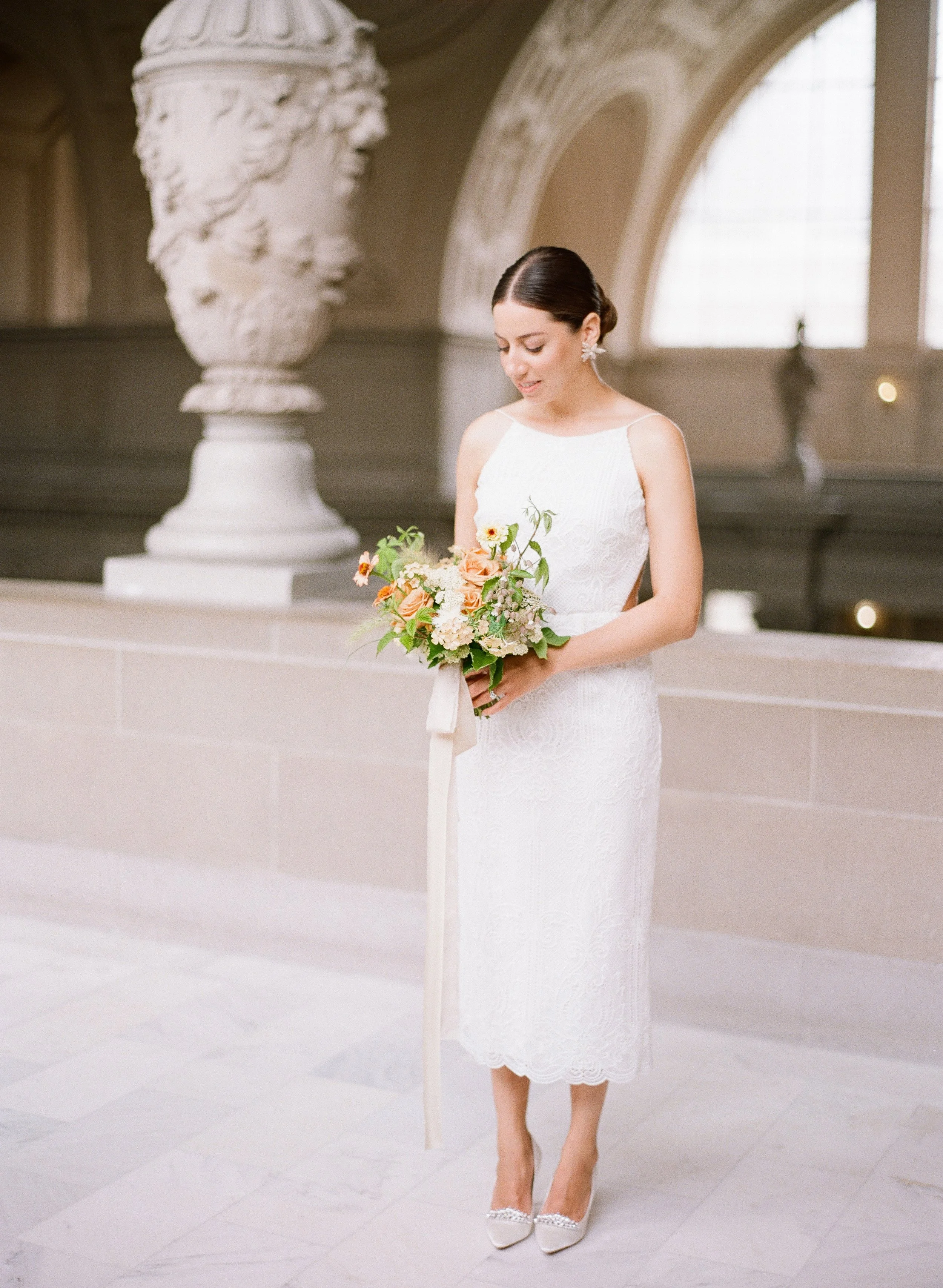 Bride in a minimal halter gown looking down at her garden rose bouquet at San Francisco City Hall, film wedding photography by Radostina Boseva