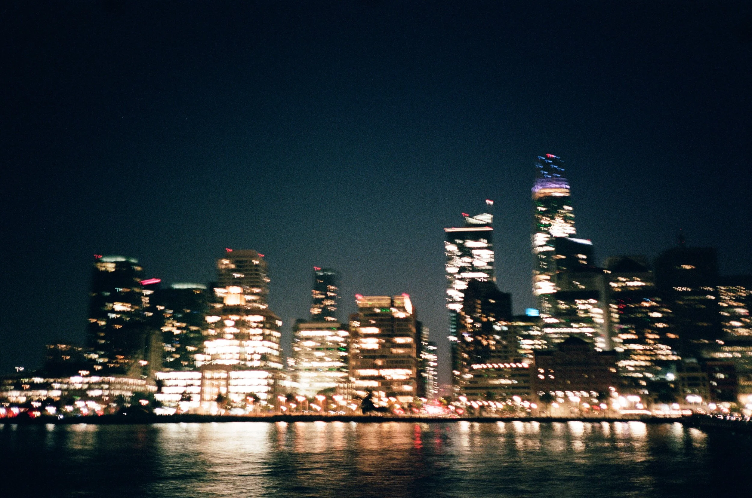San Francisco skyline at night with city lights reflected in the bay, shot on film with bokeh blur by Radostina Boseva