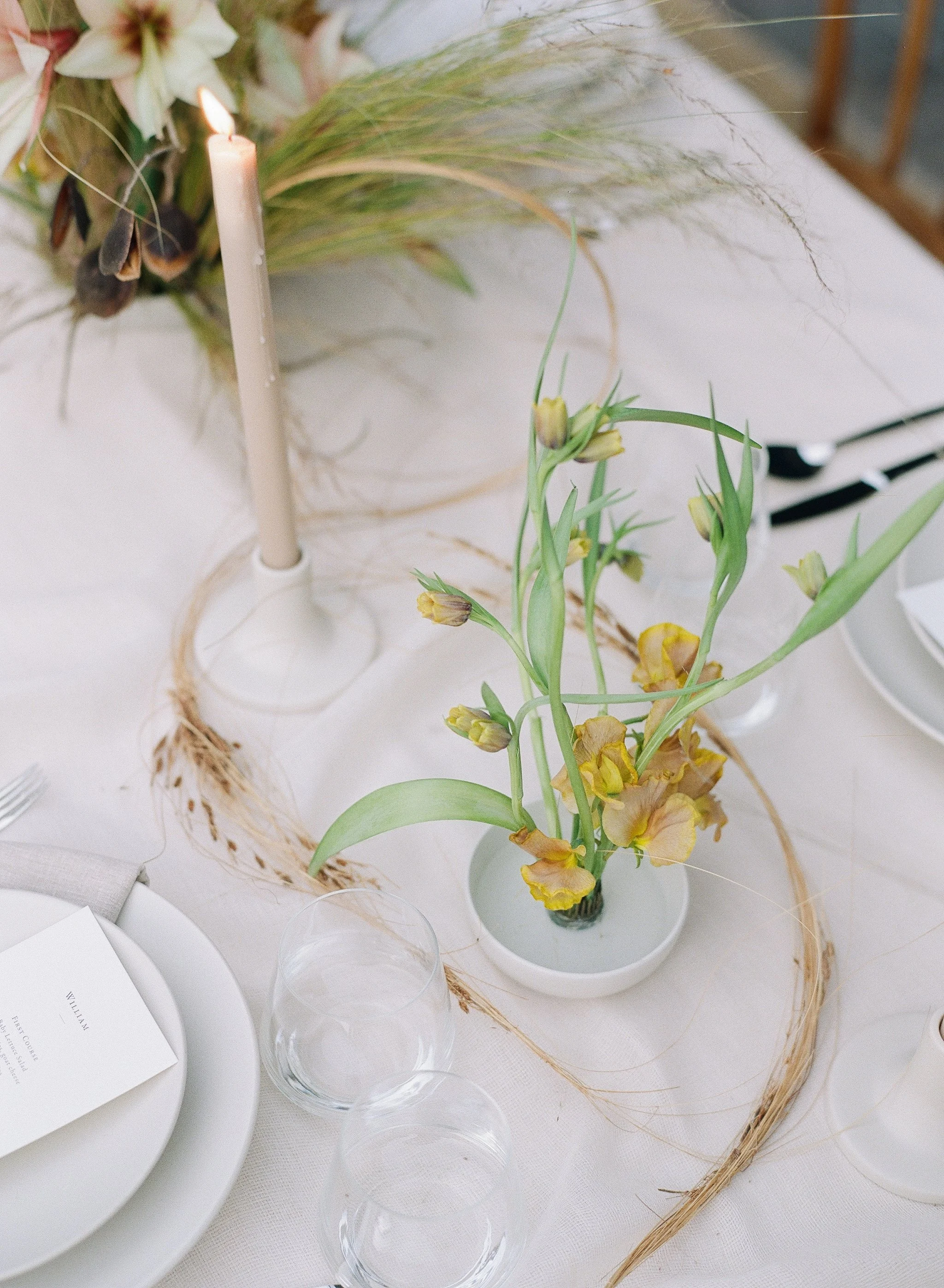 ikebana-inspired wedding table florals — sparse tulips in a low bowl beside a taper candle, on film