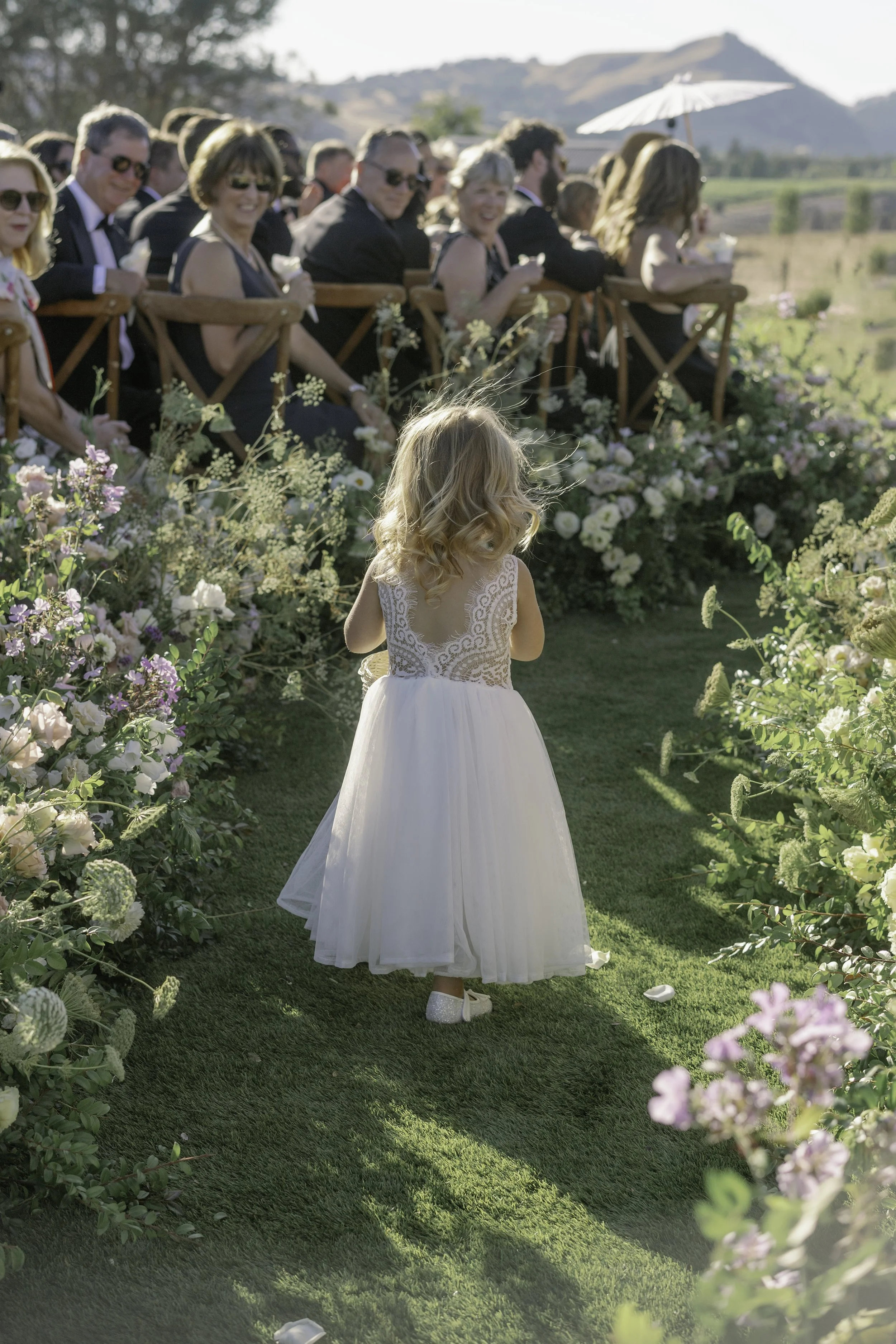 Candid documentary moment of flower girl walking down aisle at outdoor wedding ceremony — film photography by Radostina Boseva