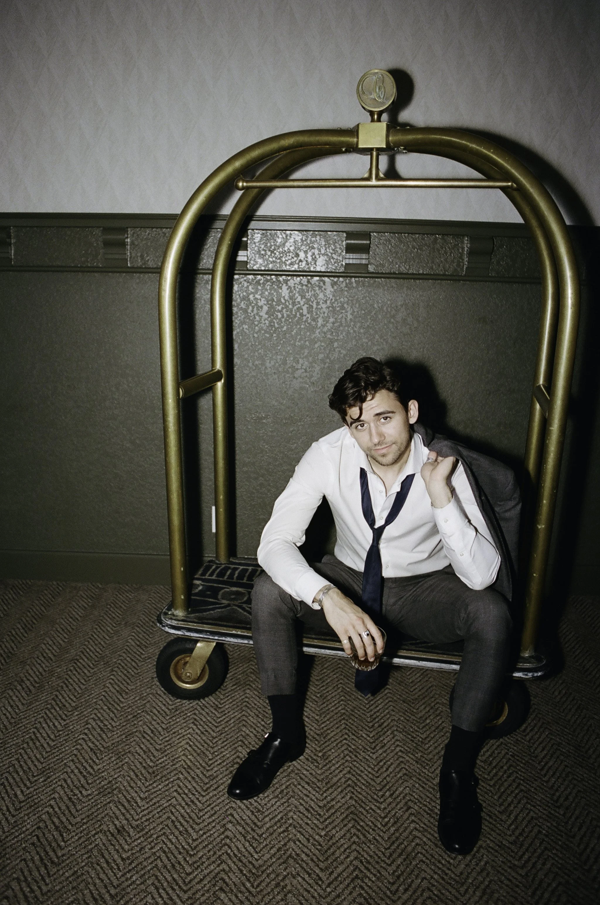 Candid documentary portrait of groom on hotel luggage cart at wedding — analogue film photography by Radostina Boseva