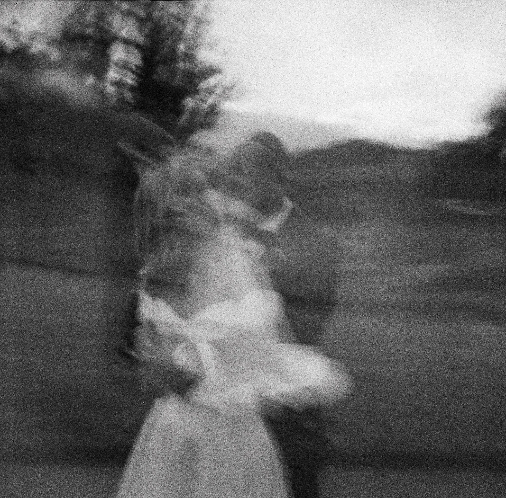 bride and groom dancing in motion blur against rolling hills at dusk, big sur california — black and white film wedding photography by Radostina Boseva