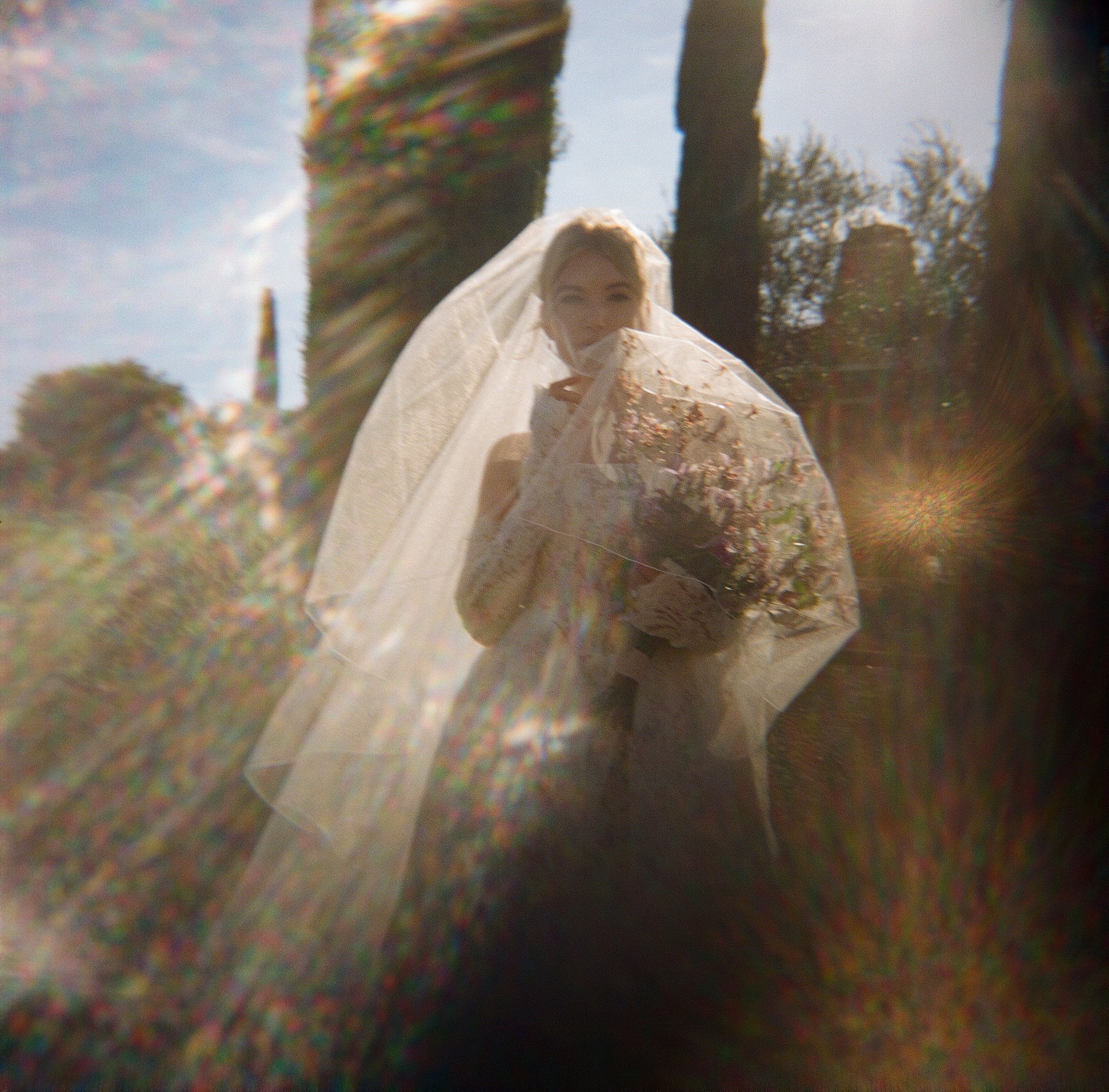 Bride in veil holding bouquet in natural light with prismatic lens flare — editorial film wedding photography, San Francisco