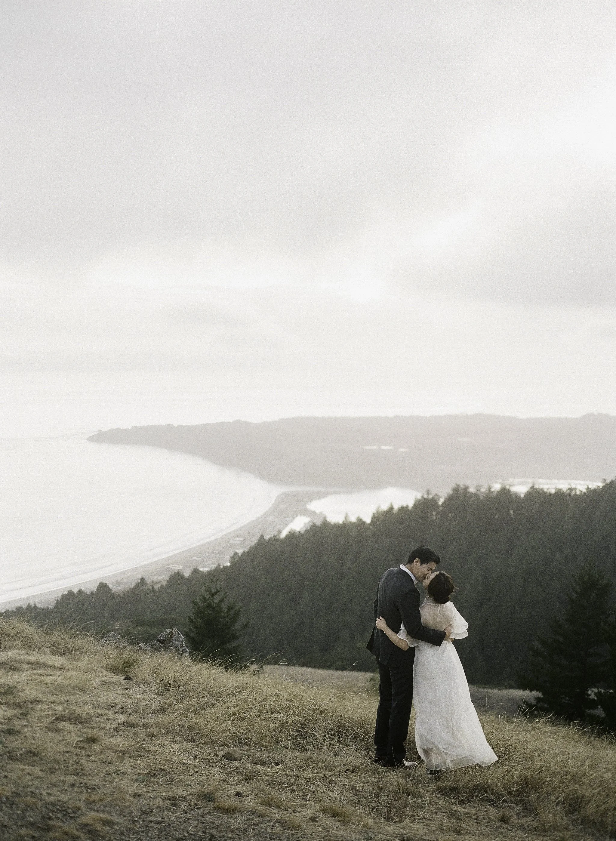 couple kissing on a grassy hilltop at dusk, coastal forest below · marin headlands elopement · documentary film photography by radostina boseva