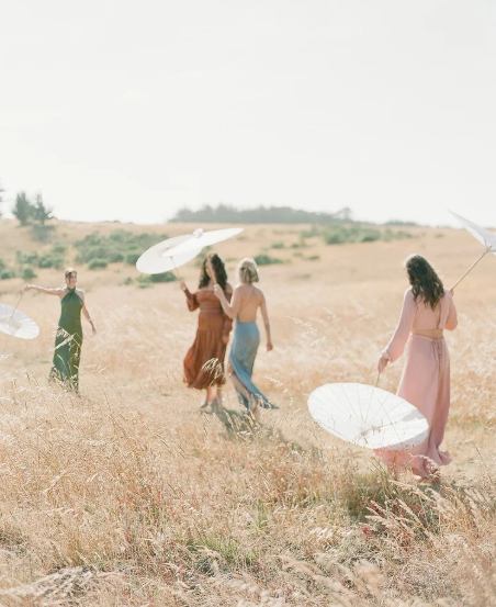 Bridesmaids in colorful dresses walking through golden grass field with parasols, photographed on film in Mendocino